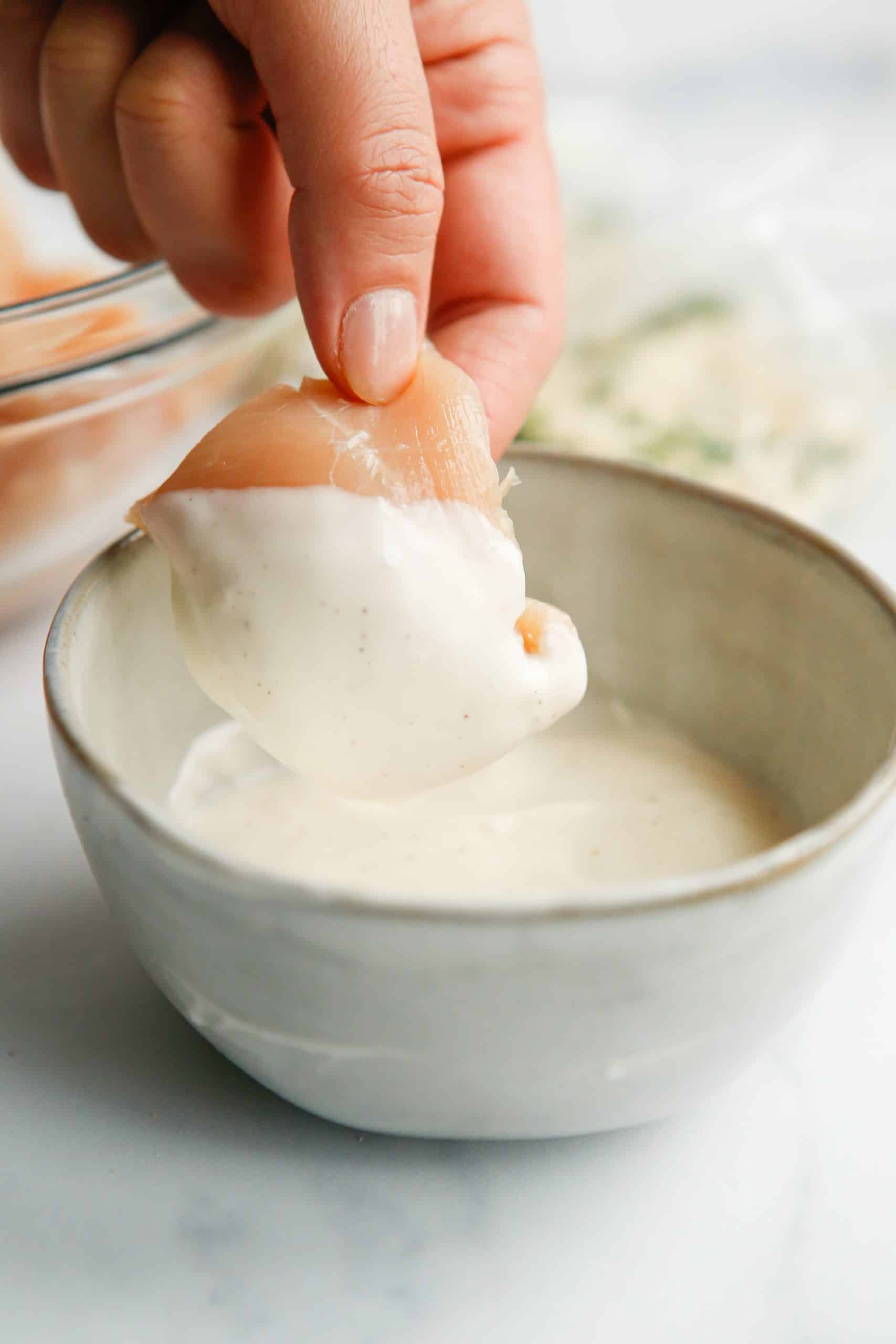 Hand dipping piece of chicken into ranch dressing in a bowl.