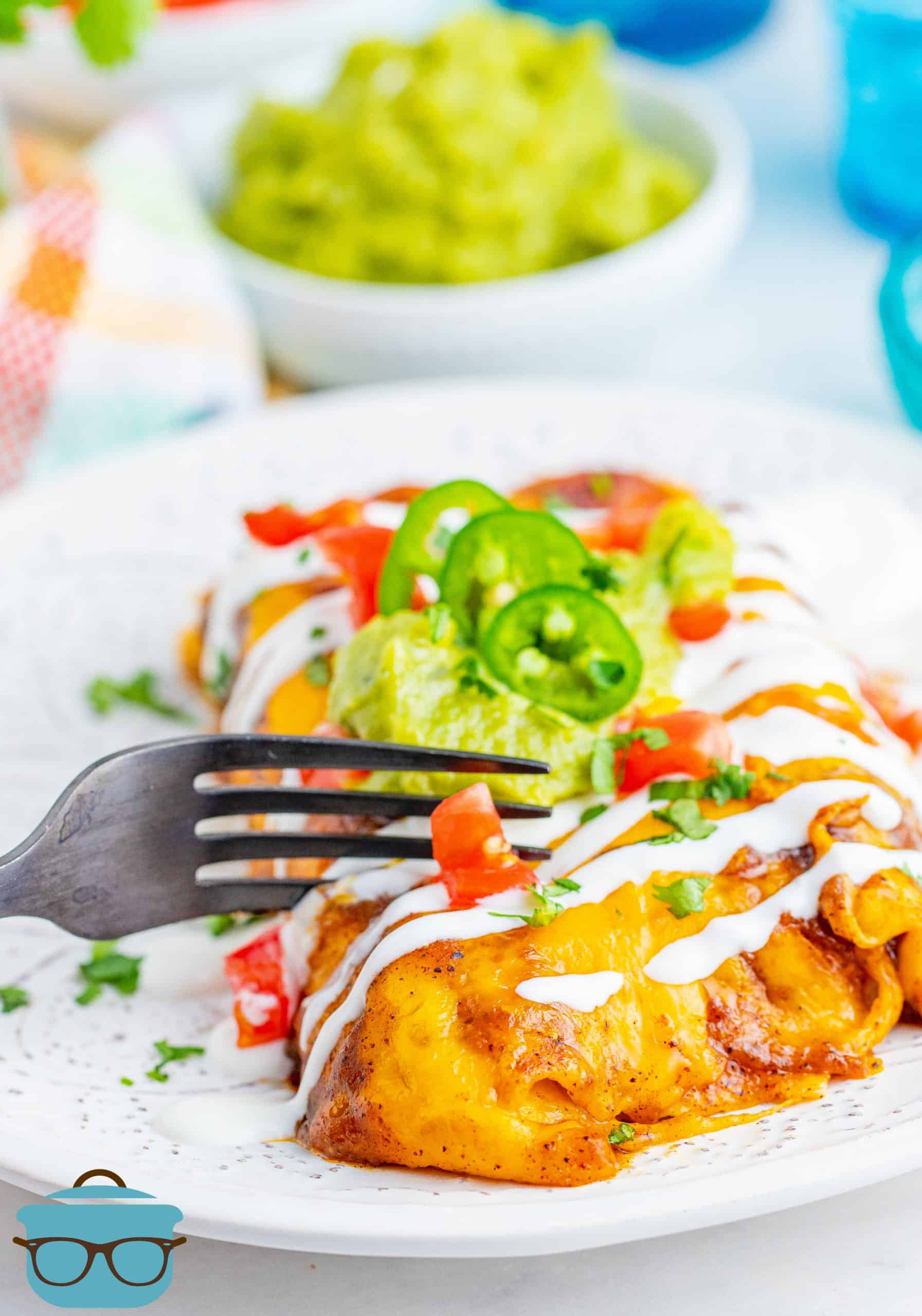 two enchiladas on a white plate with a fork slicing through one of the enchiladas.