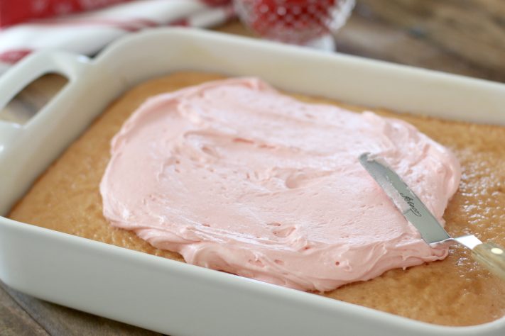 spreading pink frosting onto cake.