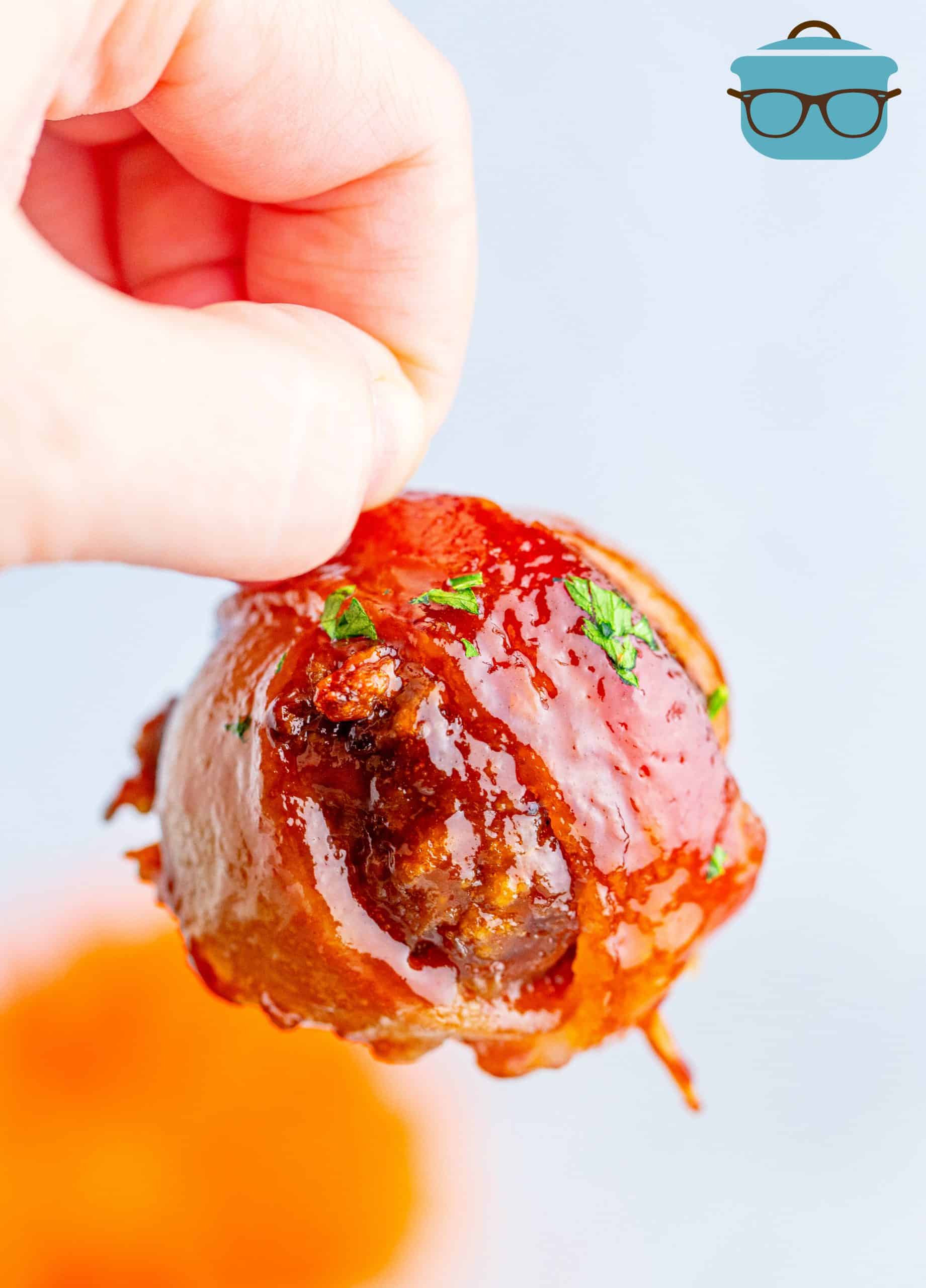 Hand holding up one Bacon Wrapped Meatball.