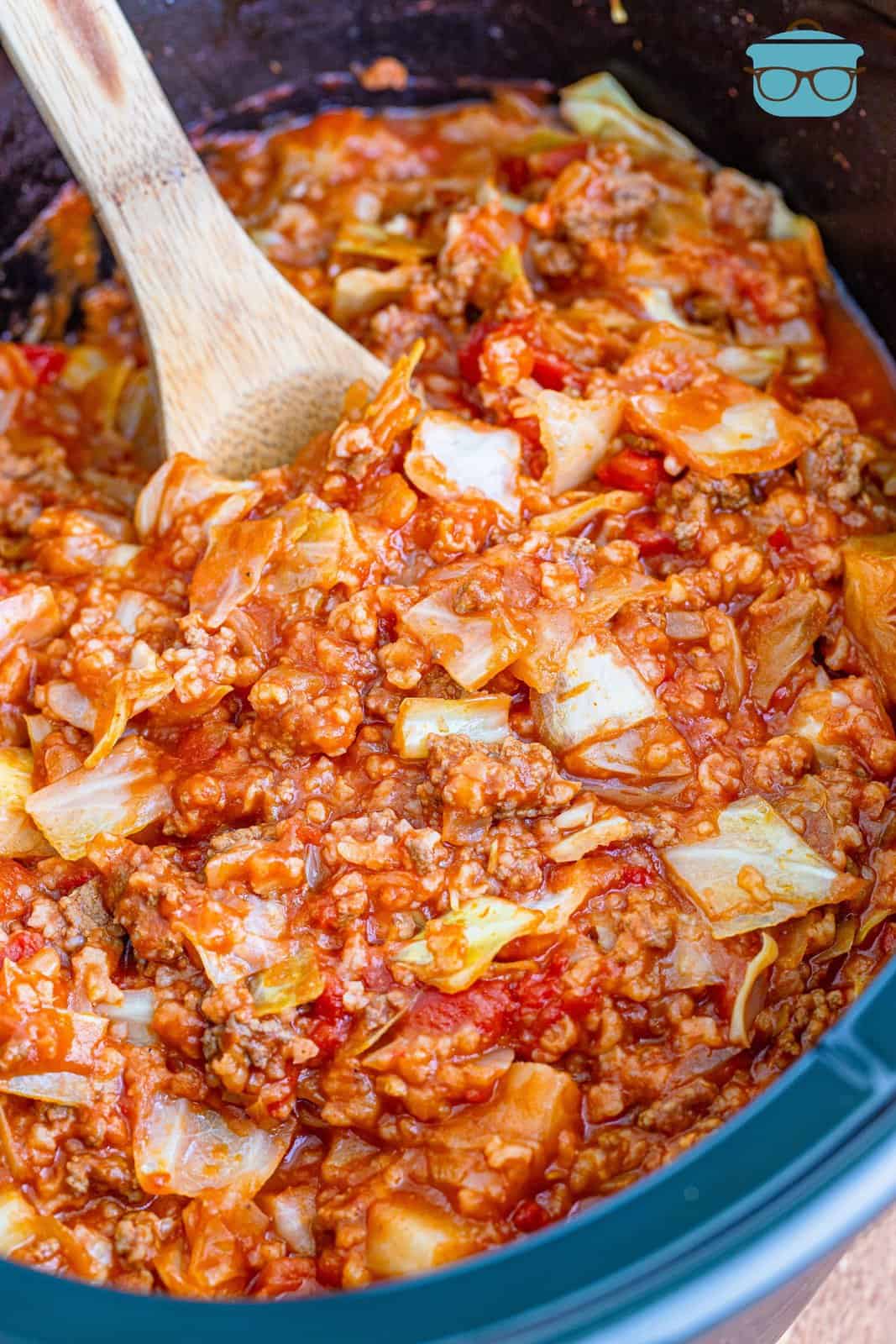 a wooden spoon inserted cooked unstuffed cabbage rolls in a slow cooker. 