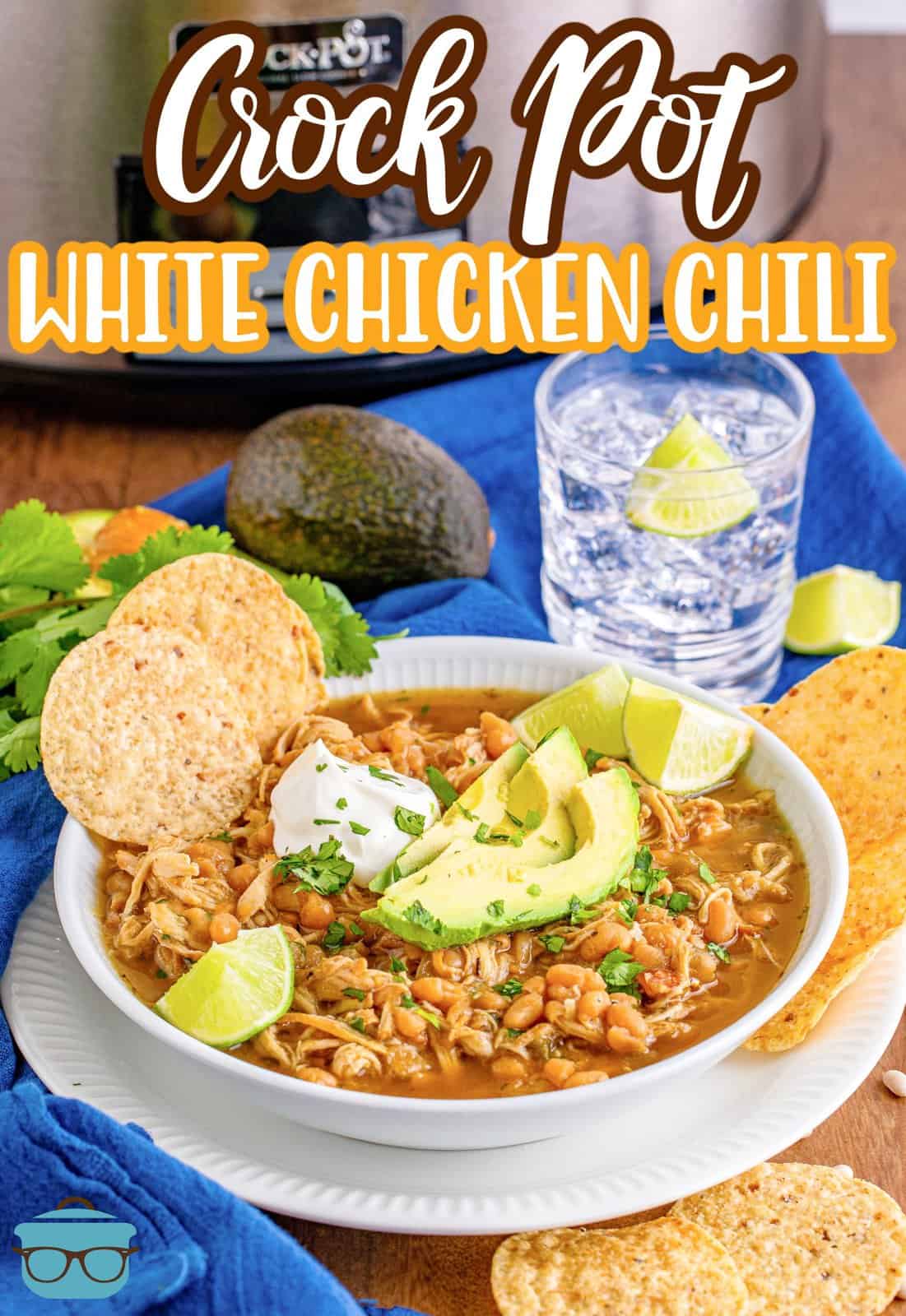 bowl of white chicken chili shown in front of a slow cooker and next to a glass of ice water. 