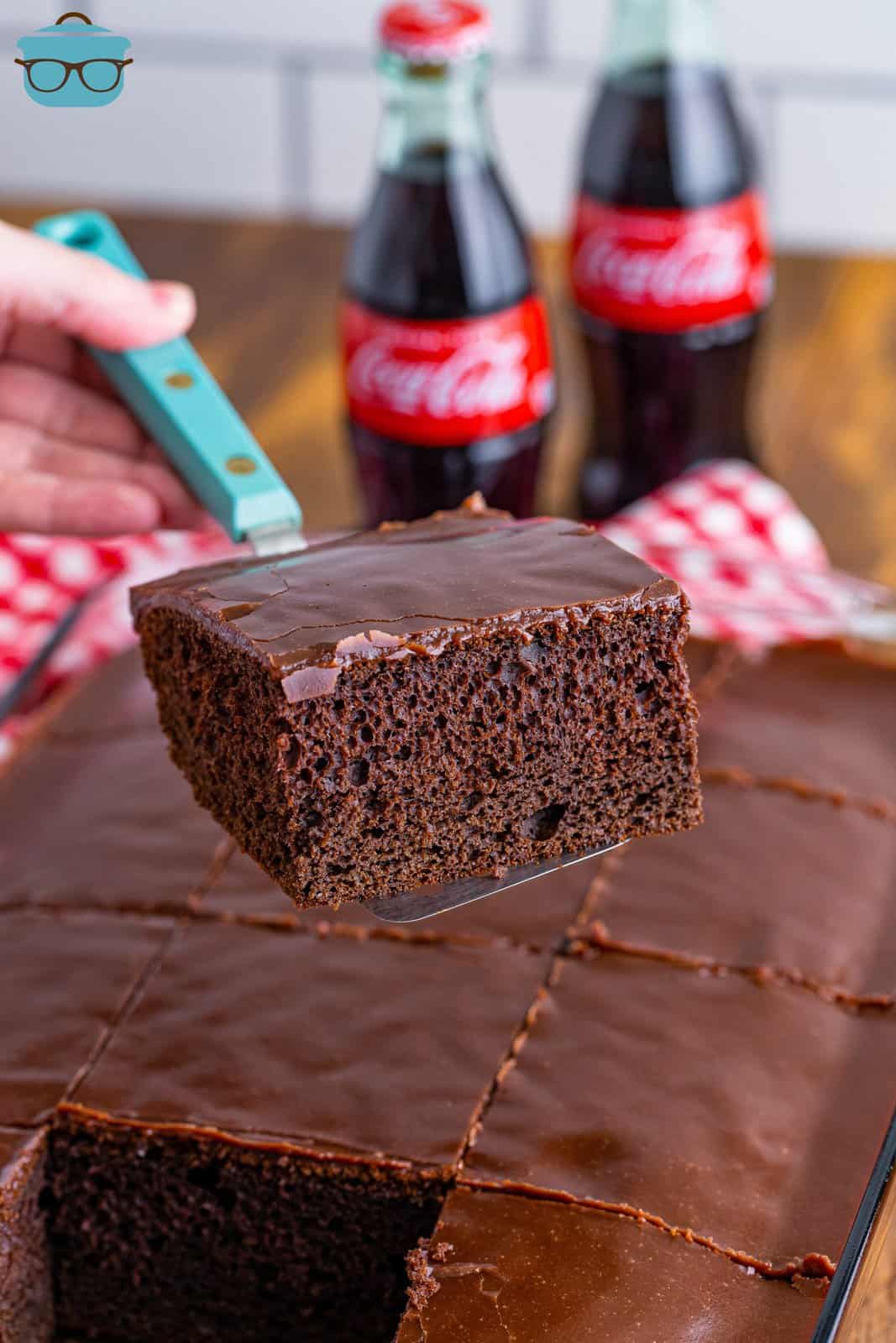 a spatula holding a slice of Coca Cola Cake over the cake pan. 