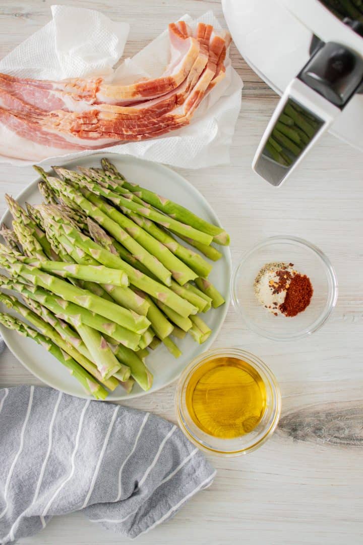 Ingredients needed to make Air Fryer Bacon Wrapped Asparagus: asparagus, olive oil, garlic powder, paprika, salt, pepper, red pepper flakes, bacon.