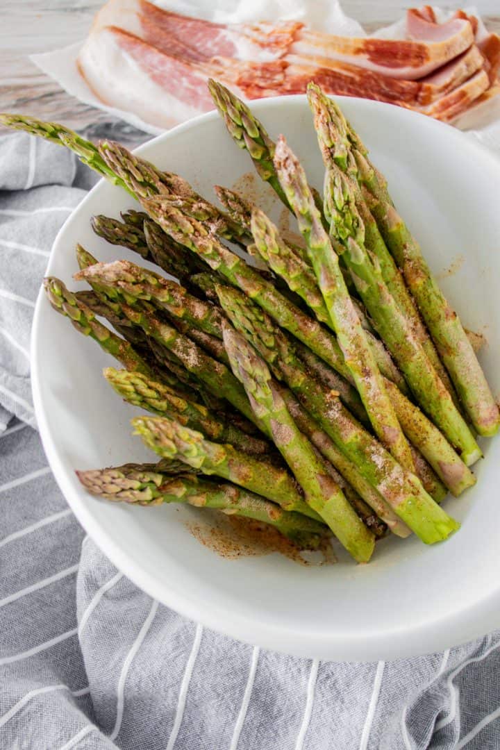Asparagus coated in seasonings and placed in a white bowl