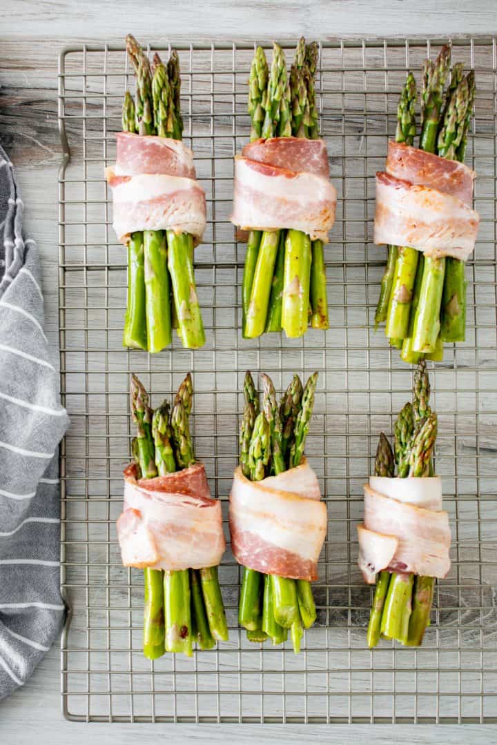 Bundles of asparagus wrapped in bacon on wire rack.