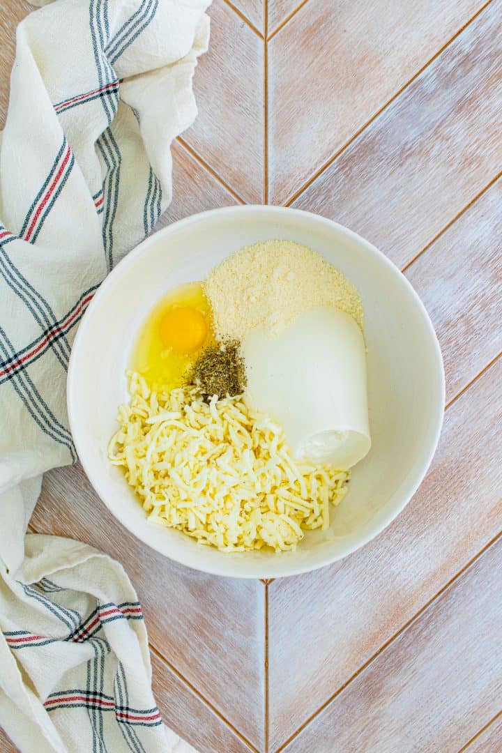 Ricotta cheese, egg, parmesan and mozzarella in a white bowl.