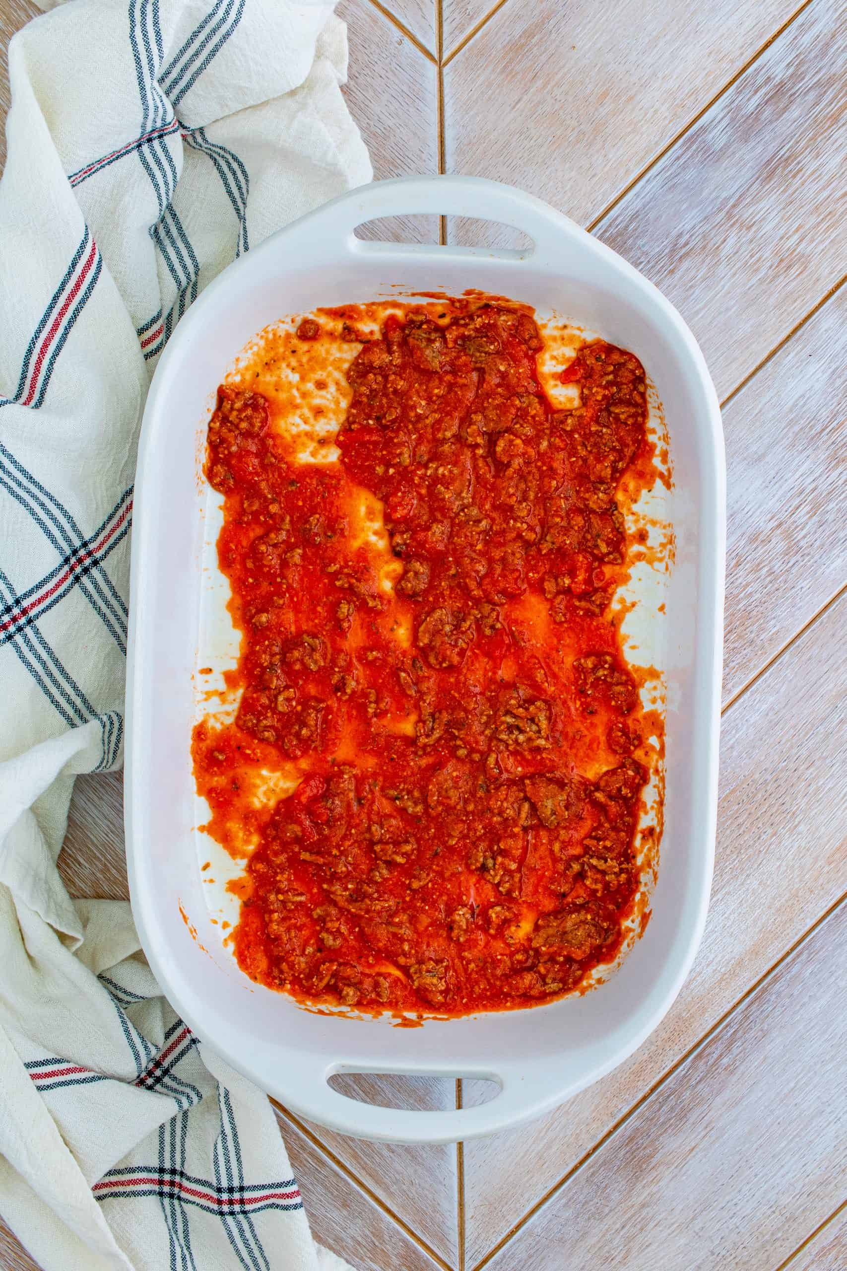 Meat sauce added to bottom of a white rectangle baking dish.