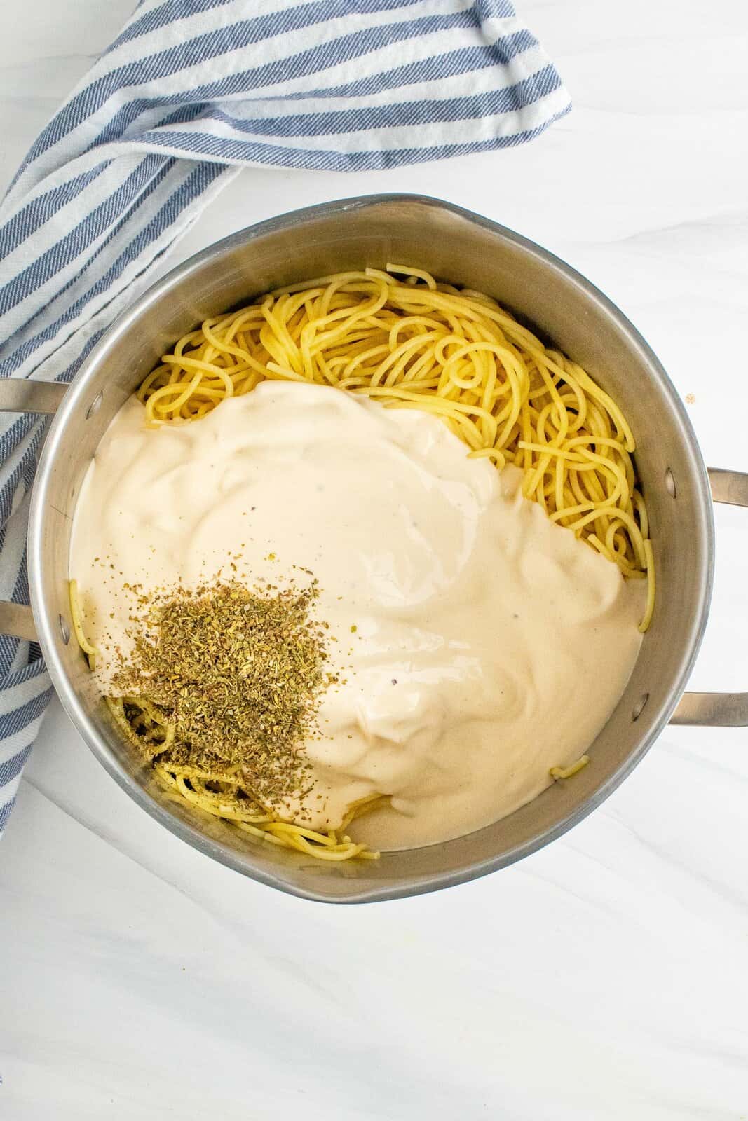 Alfredo sauce and Italian seasoning stirred together with cooked spaghetti noodles in a large stock pot.