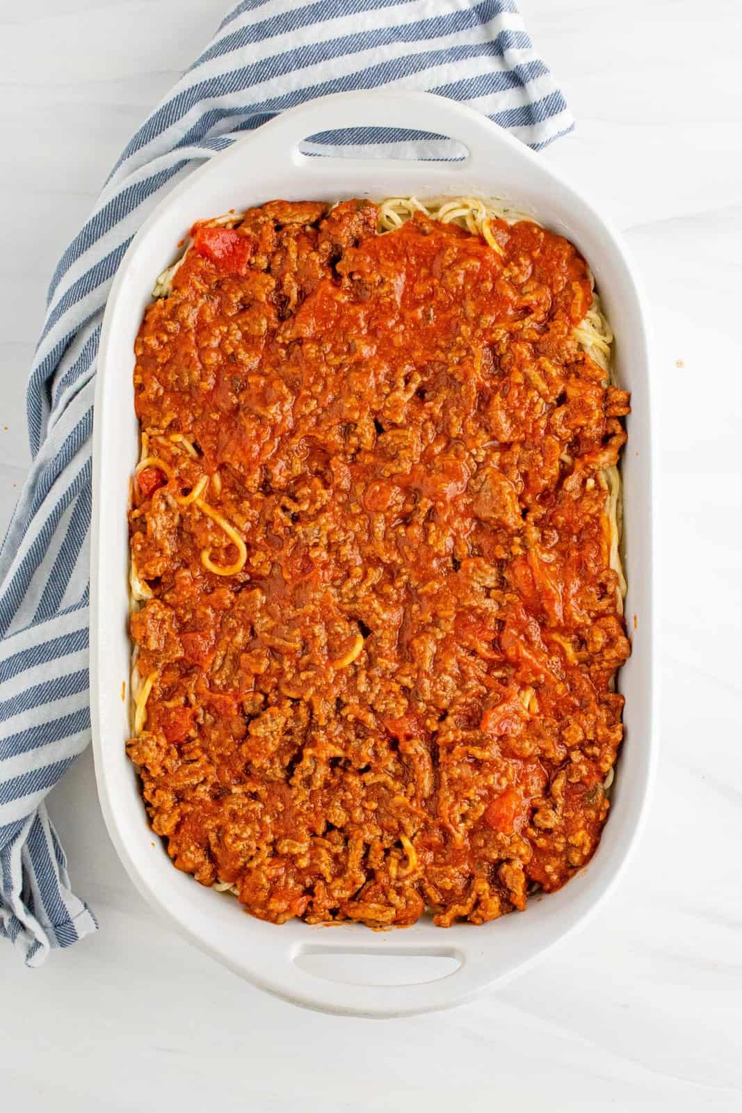 meat sauce spread on top of Alfredo noodles in baking dish.