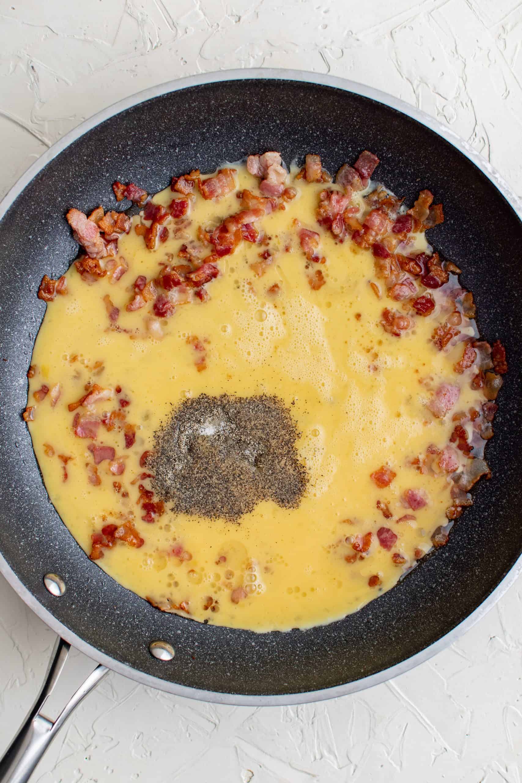 Eggs added to cooked bacon in pan.