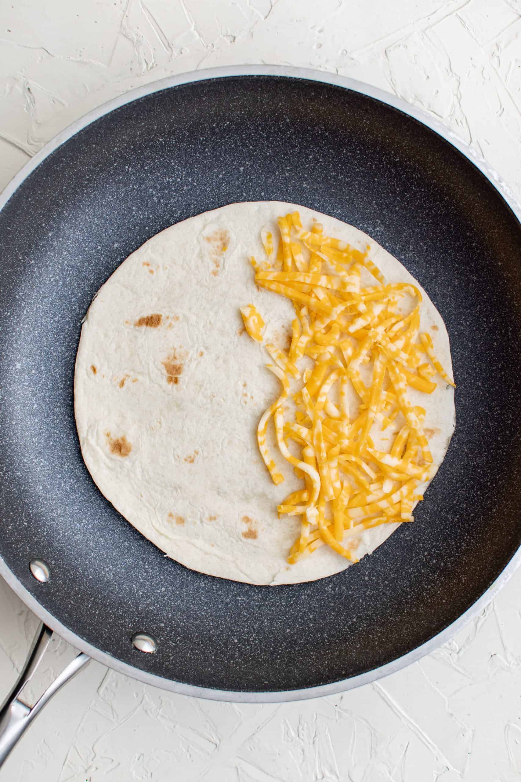 Tortilla added to pan topped with cheese on one side.