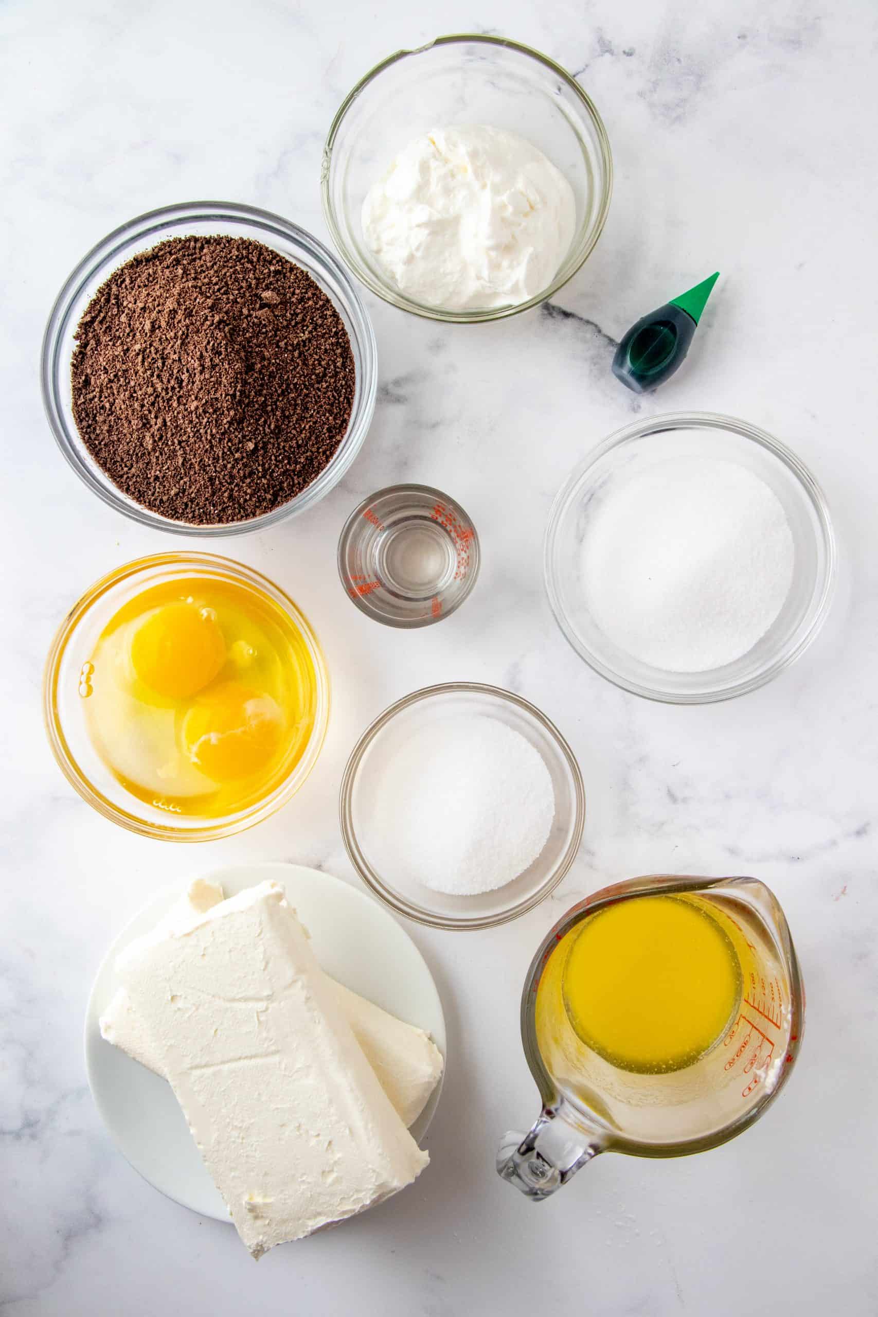Ingredients needed to make Mini Mint Chocolate Cheesecakes: chocolate graham cracker crumbs, butter, sugar, cream cheese, sour cream, eggs, mint extract, green food coloring.