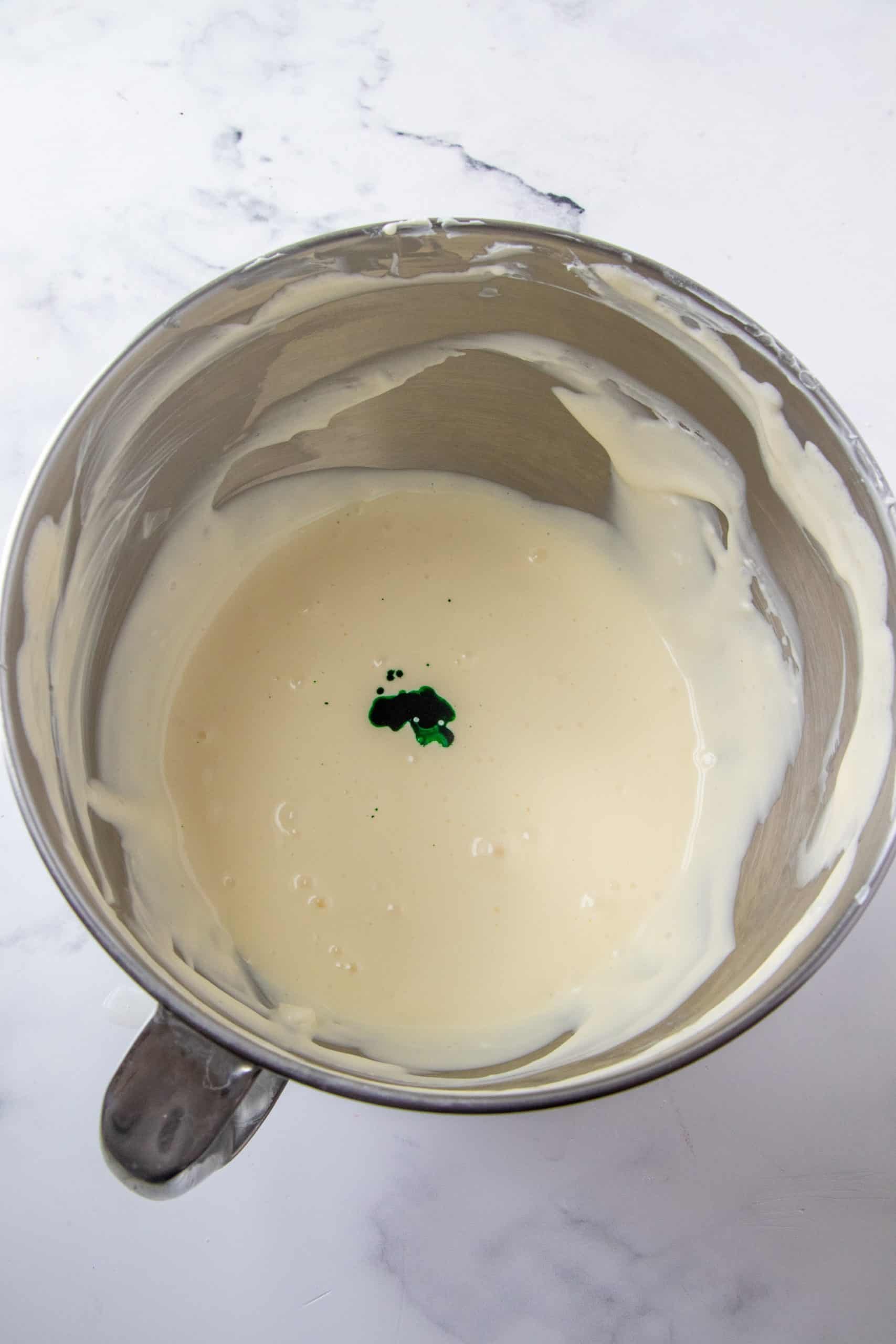 Green food color added to cheesecake batter in silver mixing bowl.