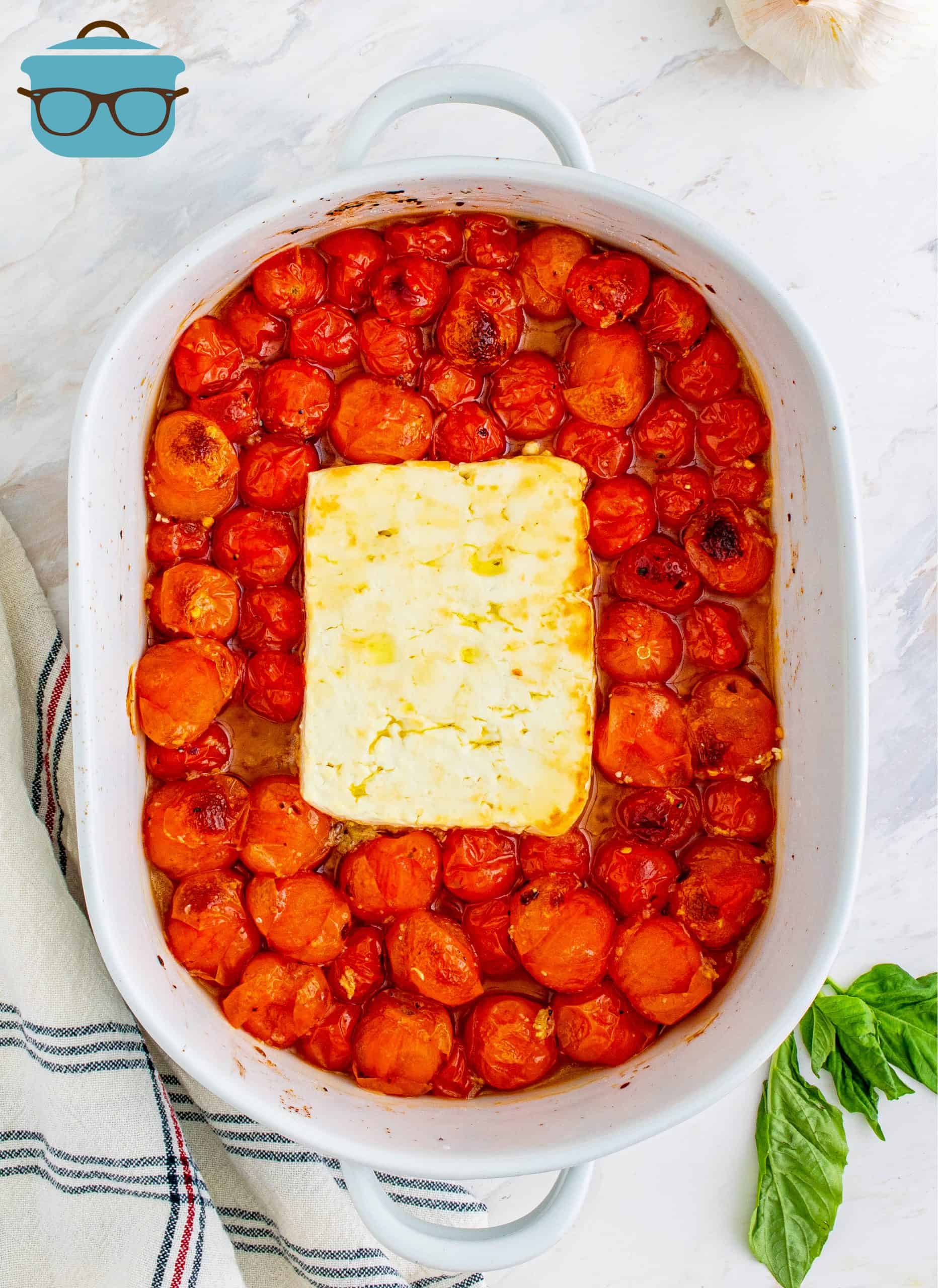 roasted feta cheese and tomatoes shown in an oval white baking dish.