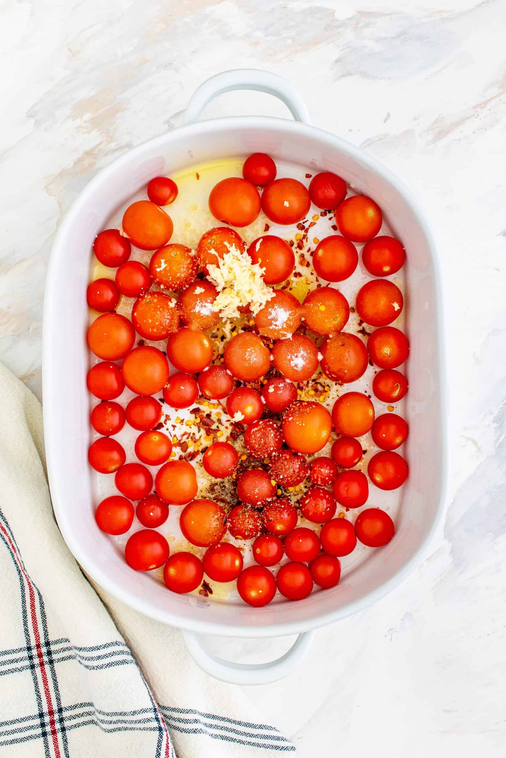 cherry tomatoes in a white round baking dish with olive oil and seasoning.