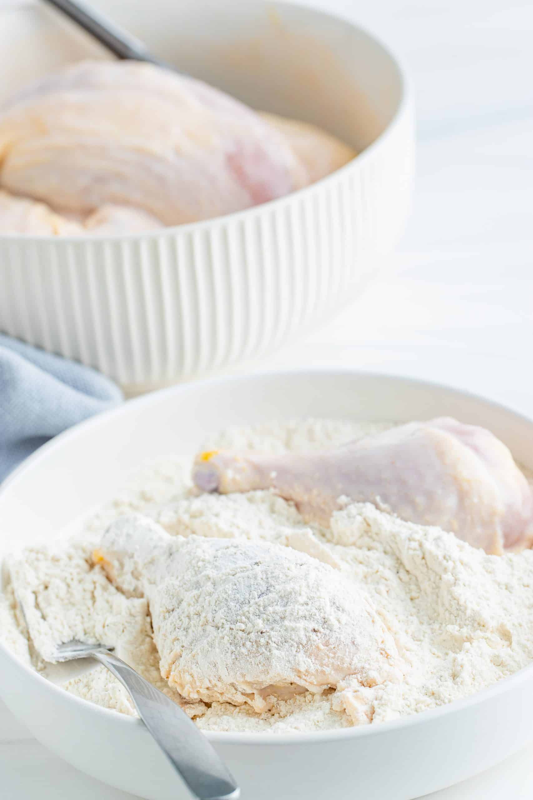 Chicken pieces being coated in flour mixture in white bowl with a fork. 