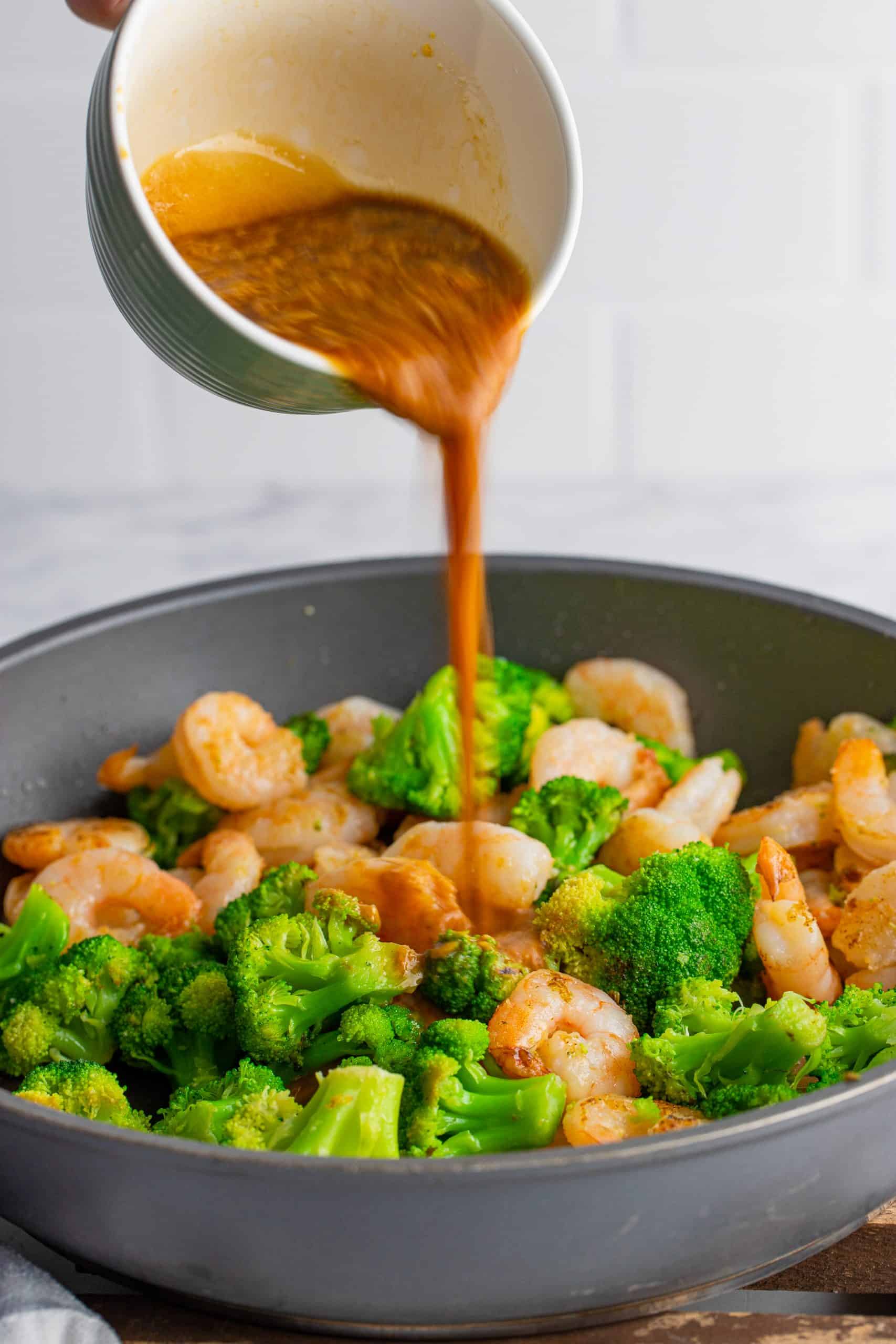 Sauce being poured over shrimp and broccoli in pan