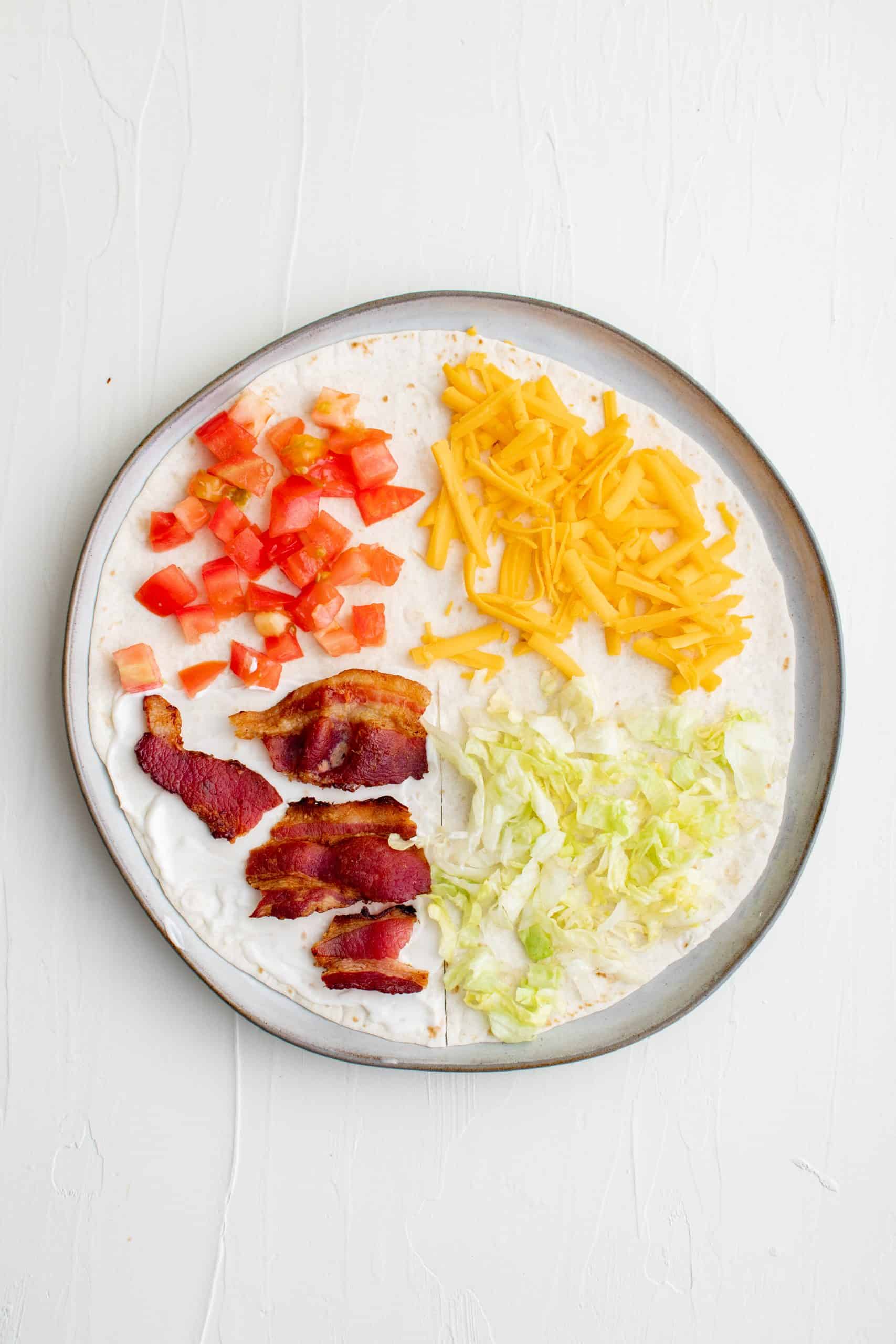 Bacon, tomatoes, cheese and lettuce on top of separate four sections of a flour tortilla.