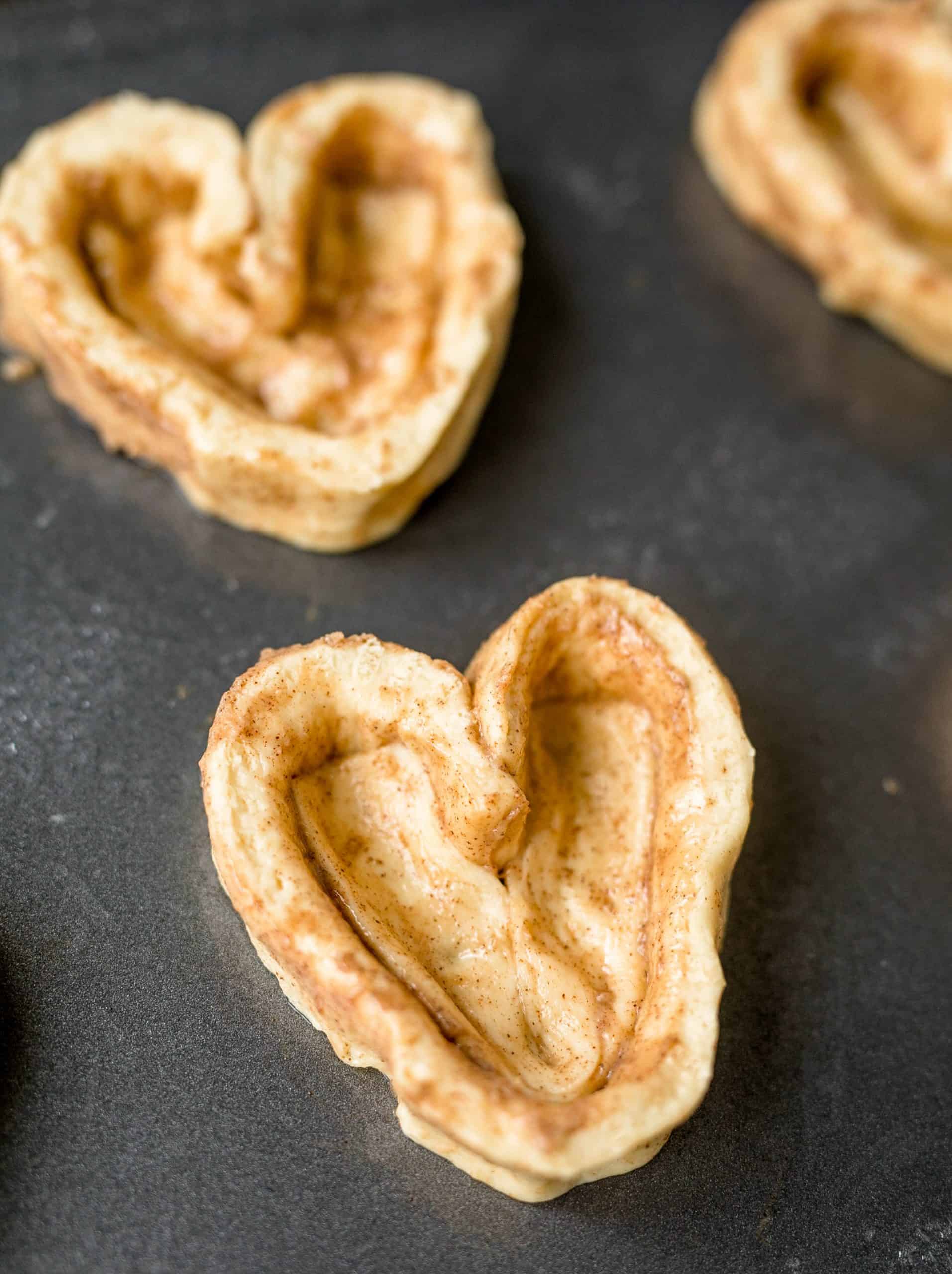 Cinnamon rolls shaped like hearts on baking sheet