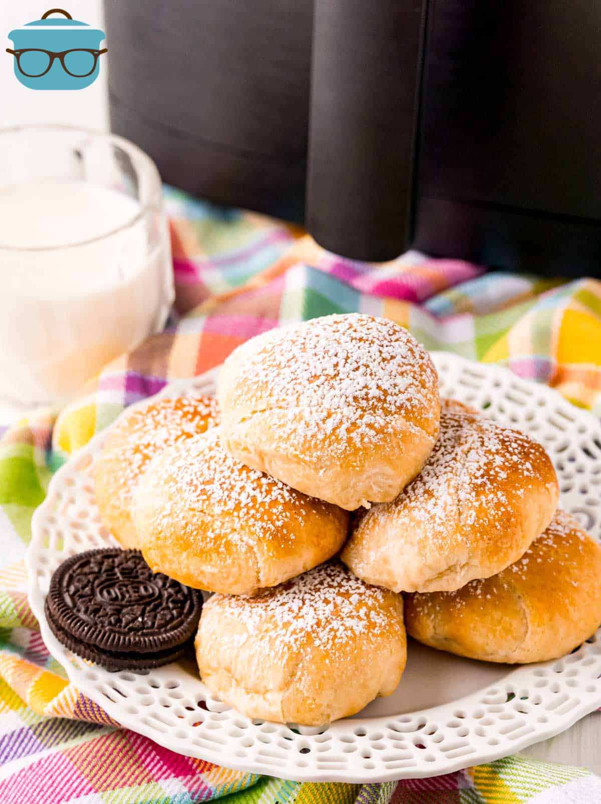 Air Fryer Fried Oreo Recipe stacked on plate topped with powdered sugar with milk next to plate.