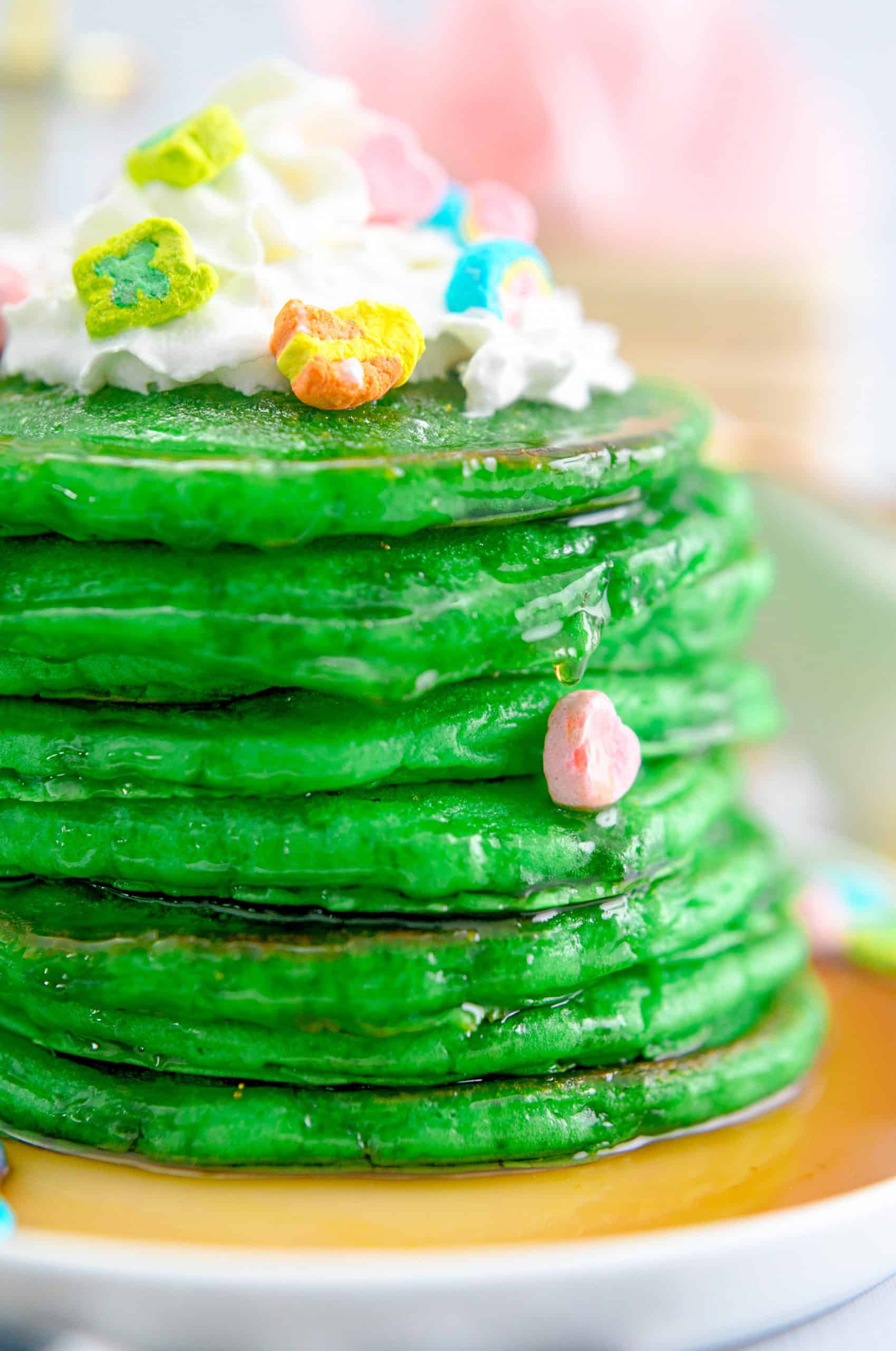 Stack of St. Patrick's Green Pancakes with syrup, whipped cream and marshmallow side view.