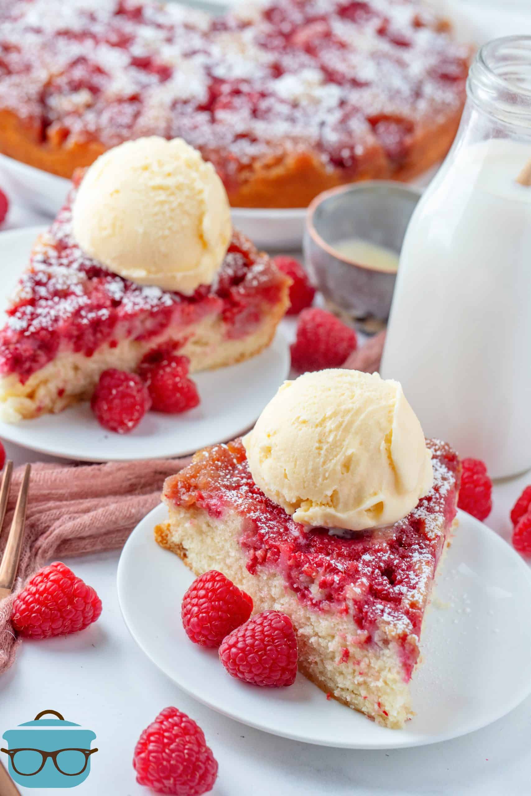 Two slices of Raspberry Upside Down Cake on white plates topped with ice cream.