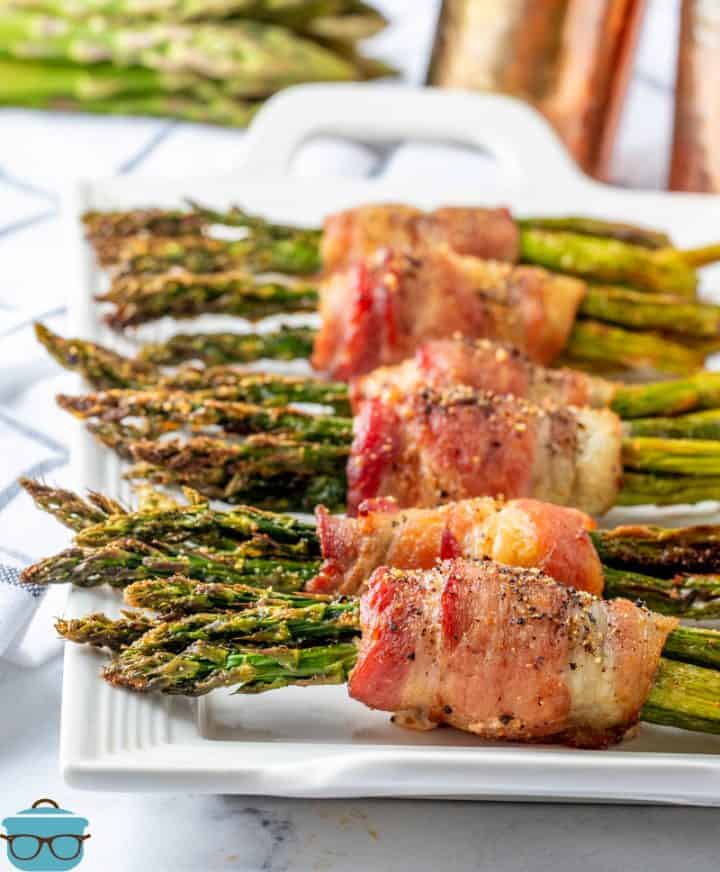 Air Fryer Bacon Wrapped asparagus lined up on a white serving tray.
