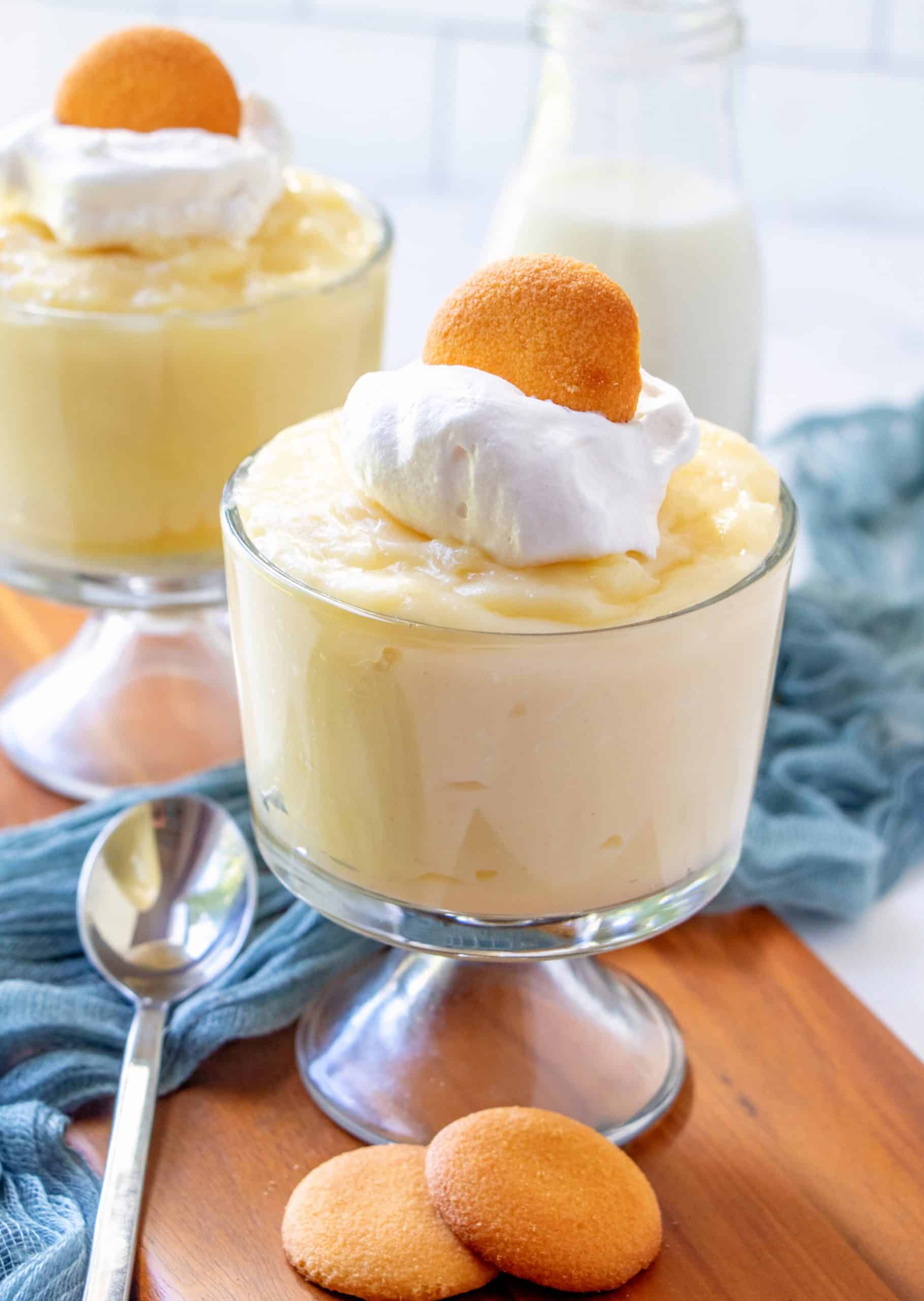 Two glass trifle cups of Homemade Vanilla Pudding topped with whipped topping and a vanilla wafer.