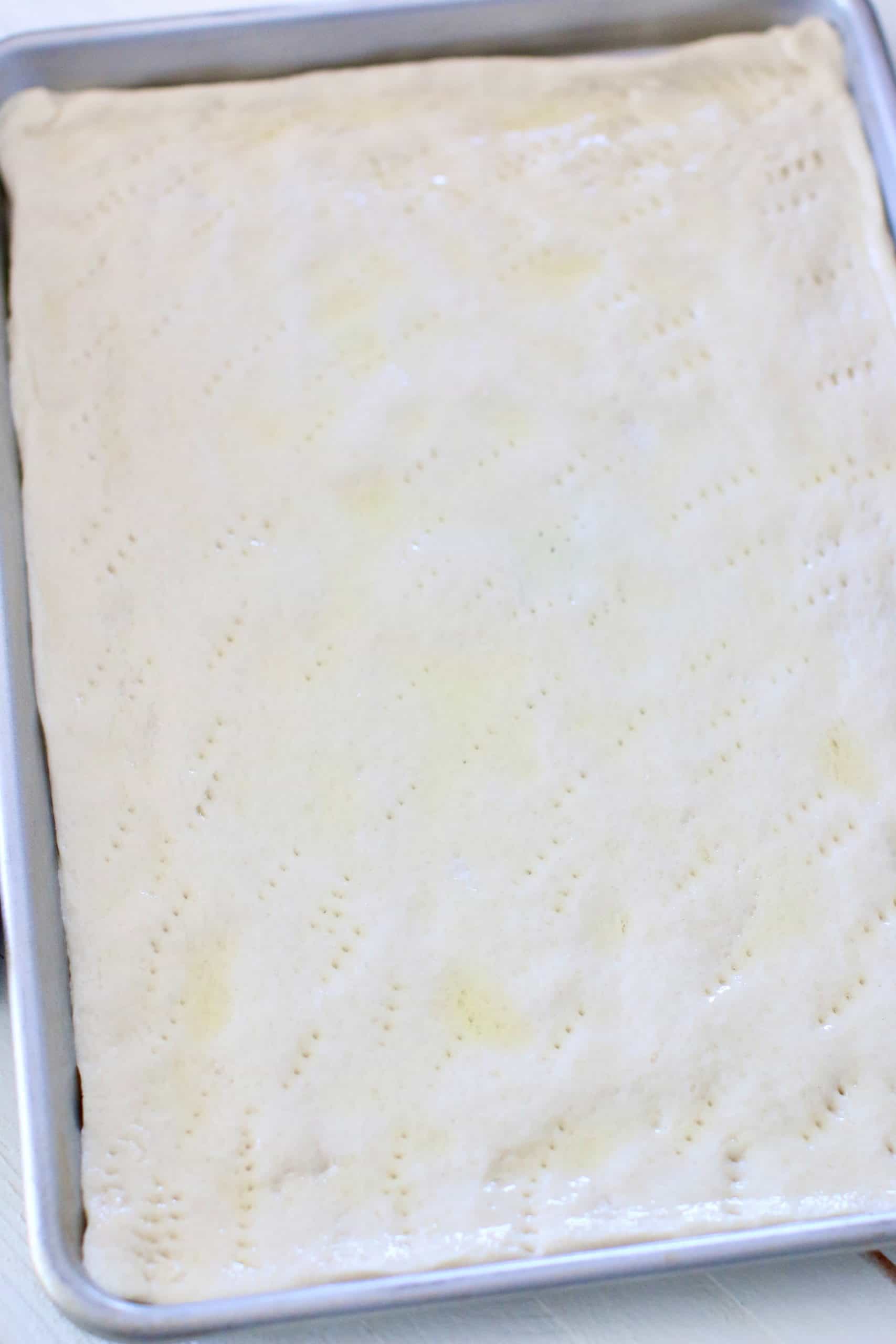 pizza dough spread out on a rectangle baking sheet.