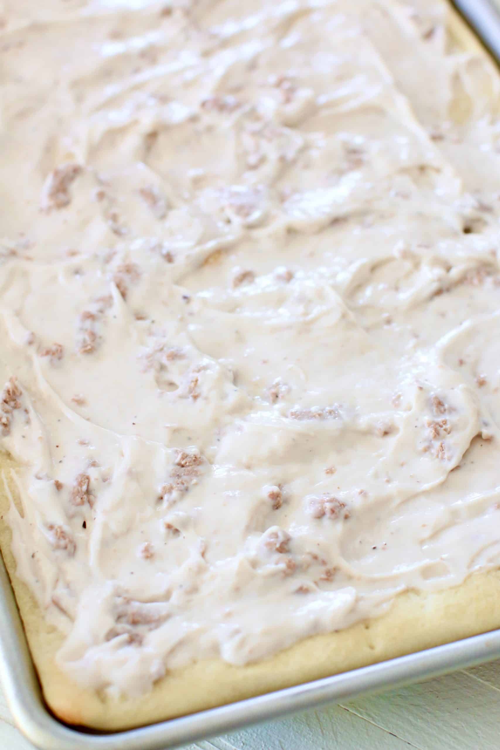 creamy white sausage gravy spread out on pizza crust in baking pan.
