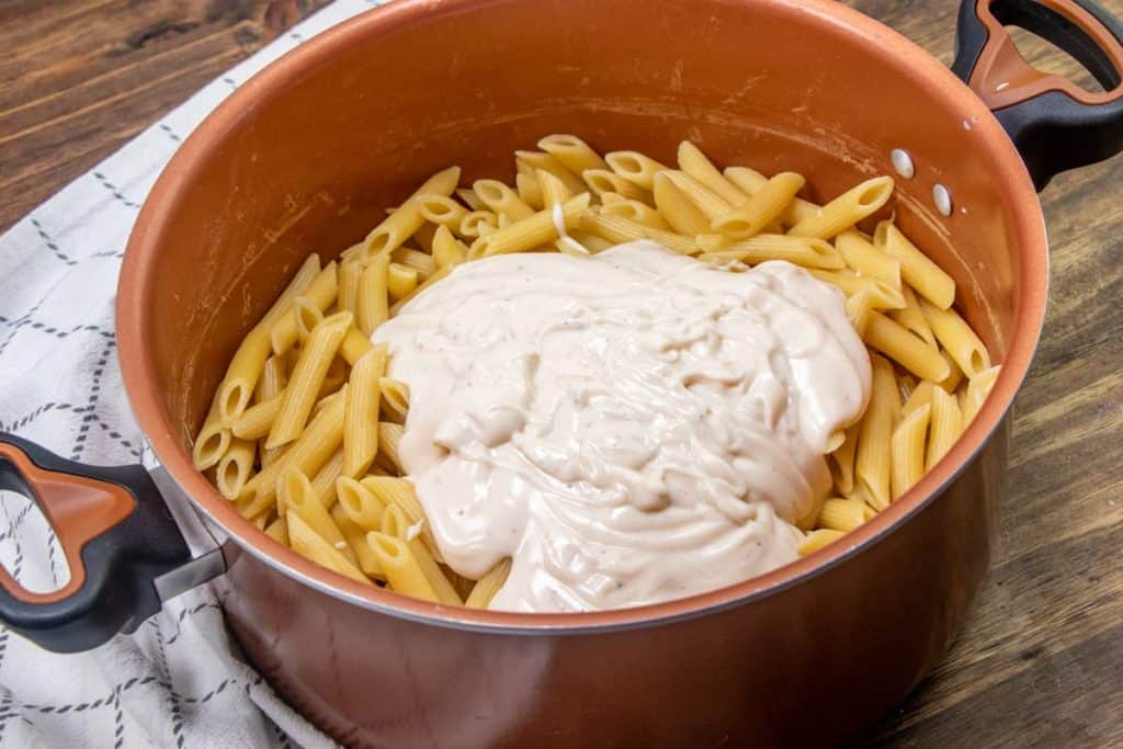 alfredo sauce added to cooked pasta in a large copper colored pot