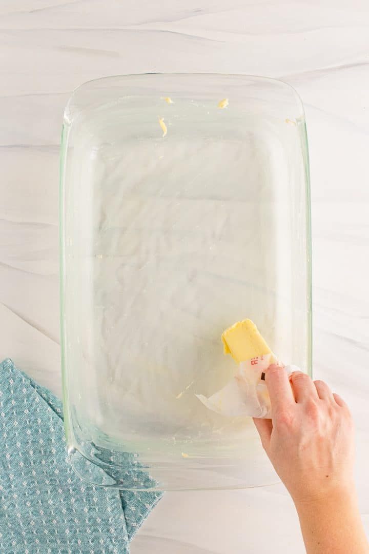 Hand buttering baking dish with a stick of butter.
