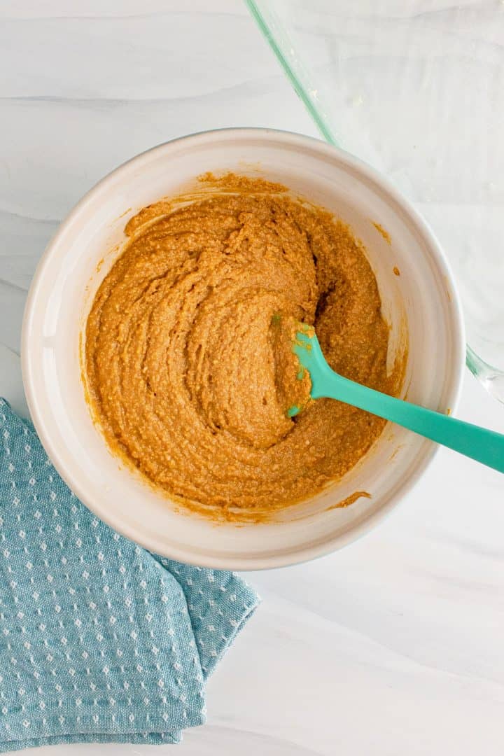 Peanut butter mixture being stirred in bowl with an aqua colored spatula.