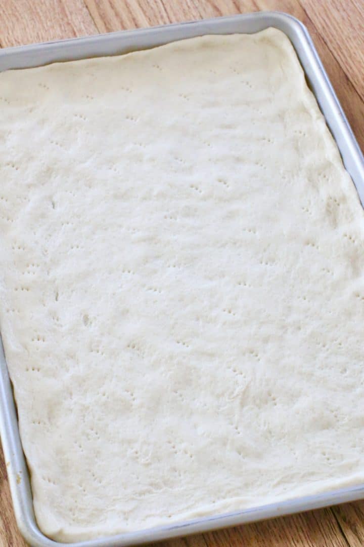 pizza crust spread out onto a rectangle baking sheet