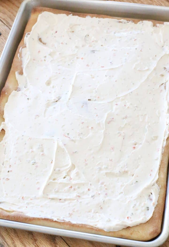 vegetable cream cheese spread evenly over a baked pizza crust in a baking pan