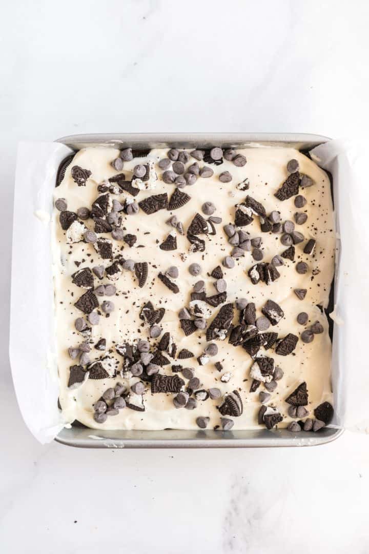 Chopped Oreos and chocolate chips topping cheesecake layer in baking pan.