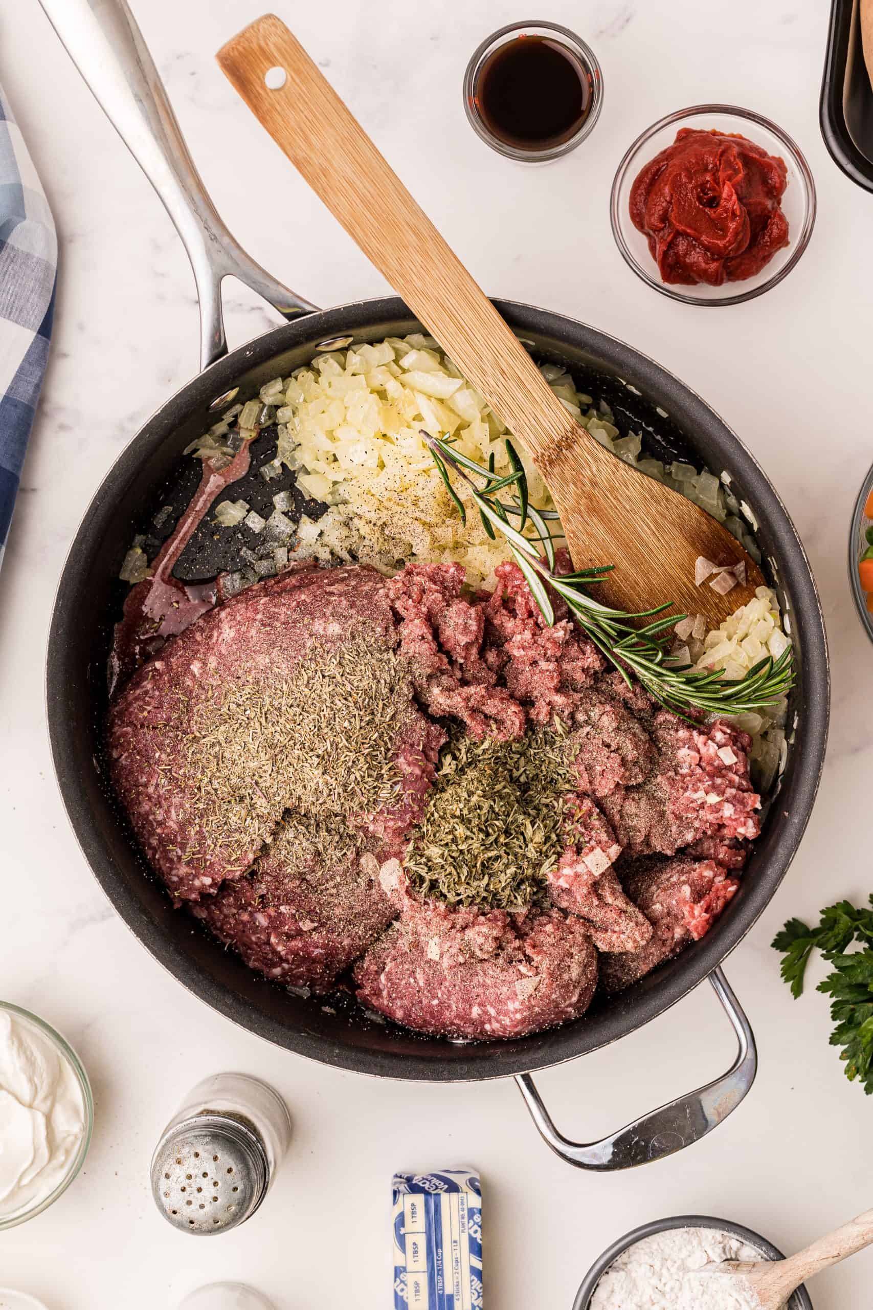 Ground meat and herbs added to onions in a skillet.