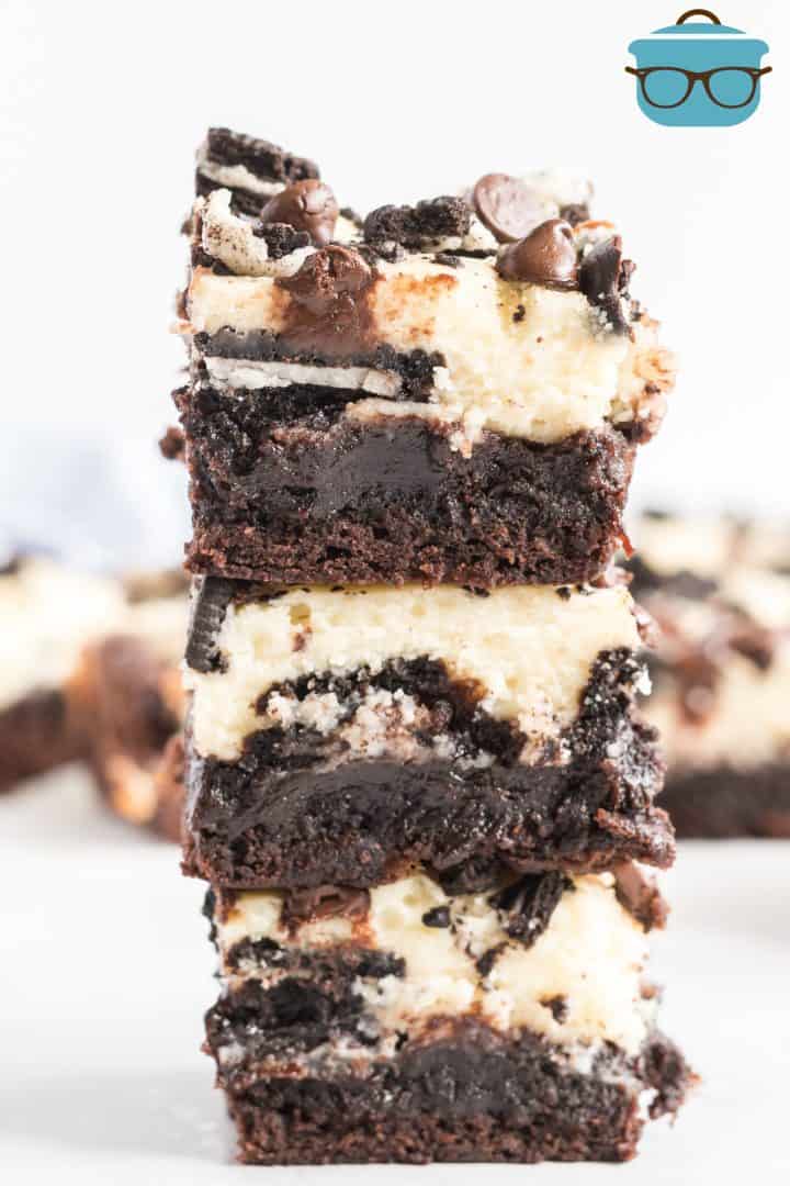 Three stacked Oreo Cheesecake Brownies on a white surface.