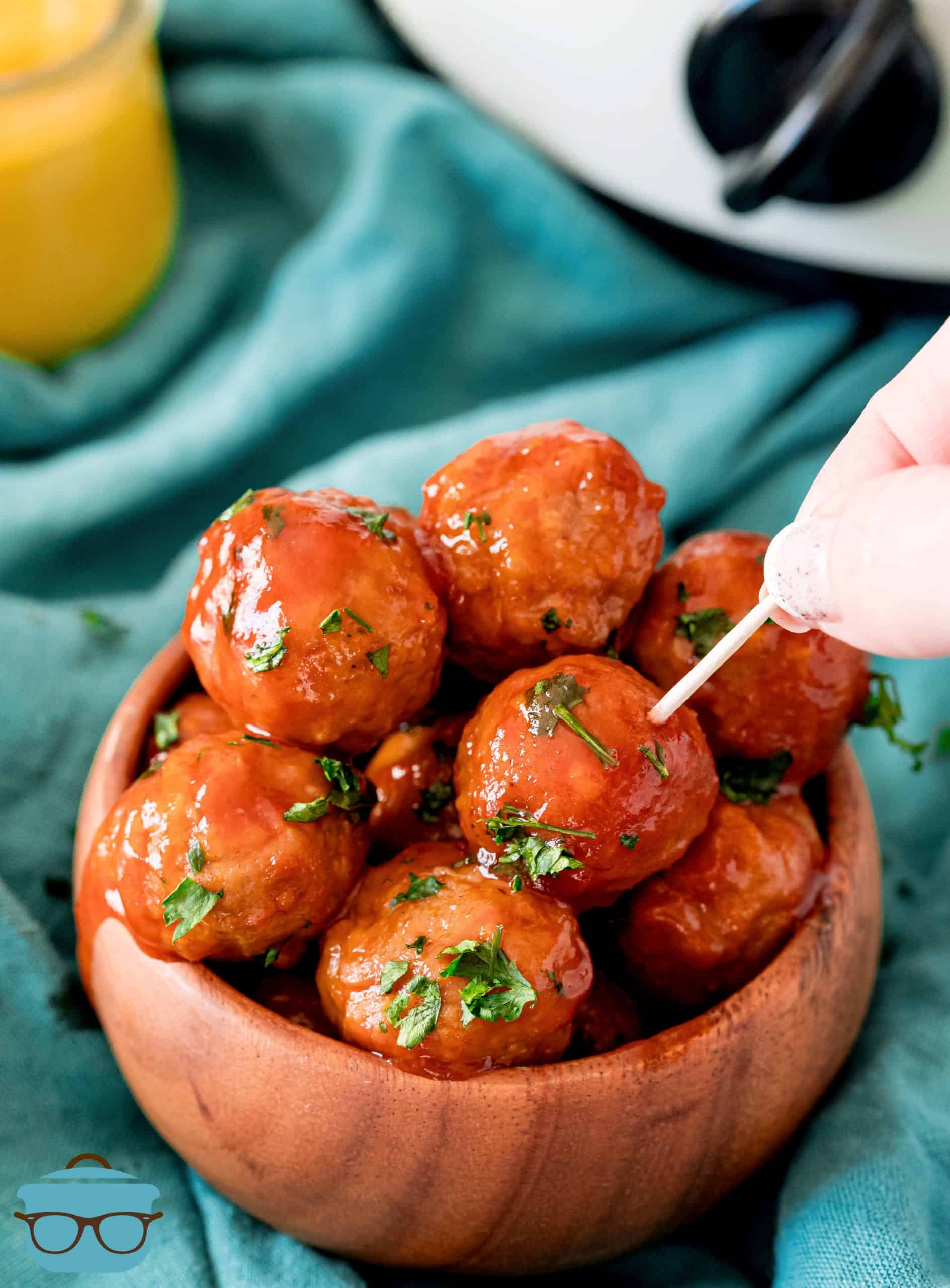 Crock Pot Meatballs in bowl with hand poking one meatball with toothpick