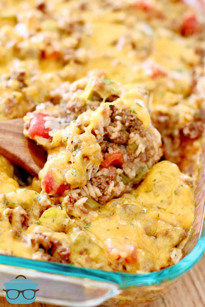 Fully cooked Stuffed Pepper Casserole shown topped with melted cheddar cheese and a wooden spoon inserted into the casserole dish.