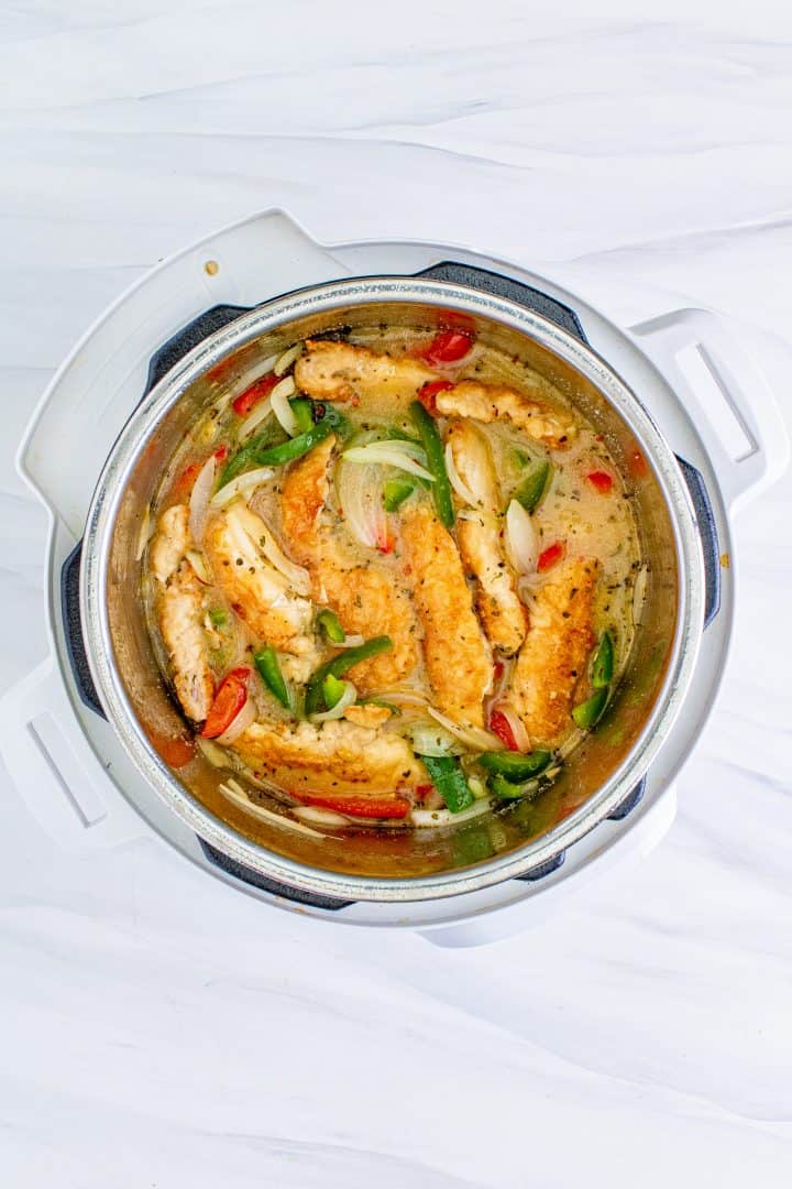 chicken tenders placed back into the instant pot with the onions and peppers.