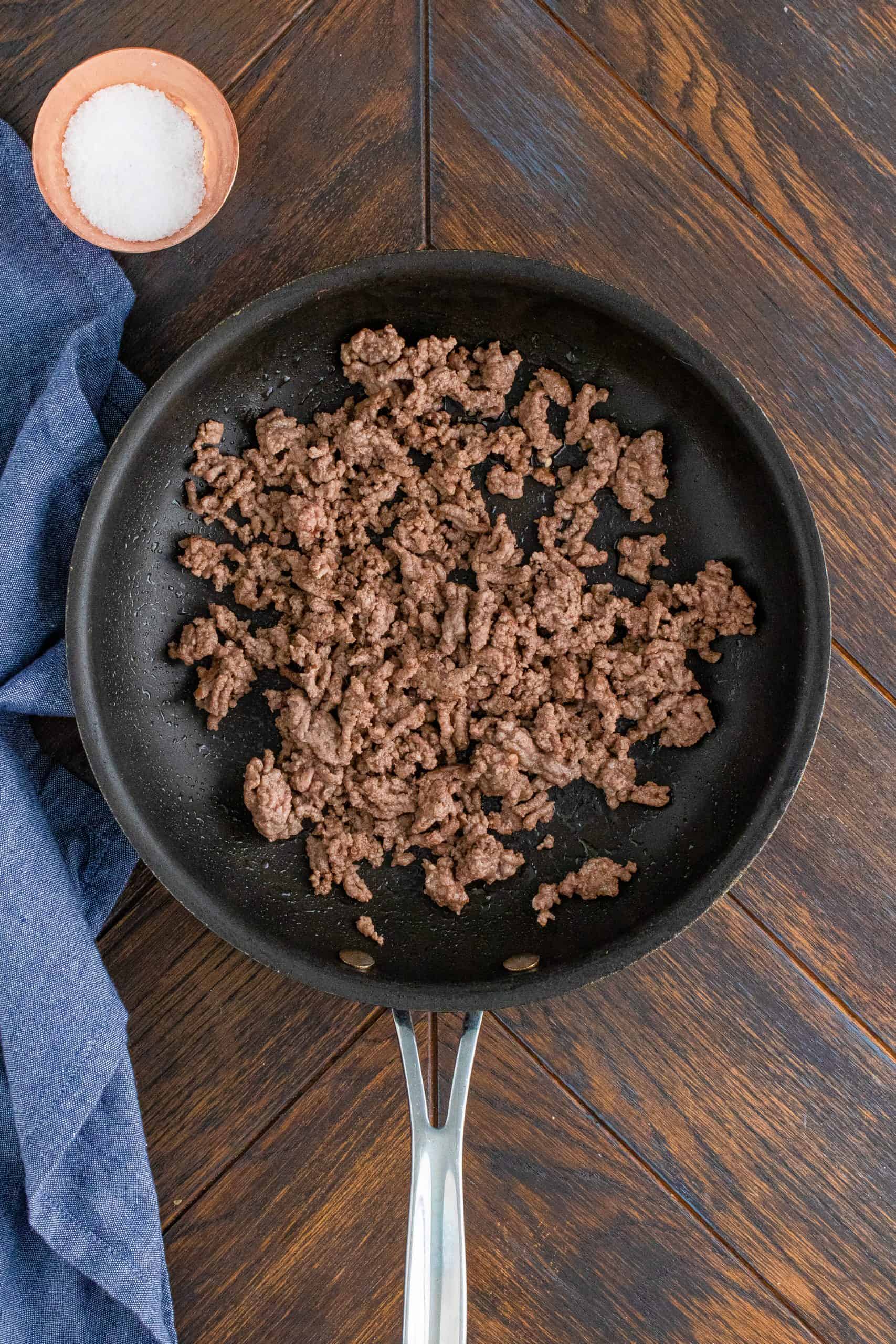 Cooked ground beef in pan with blue linen on the side of the pan.