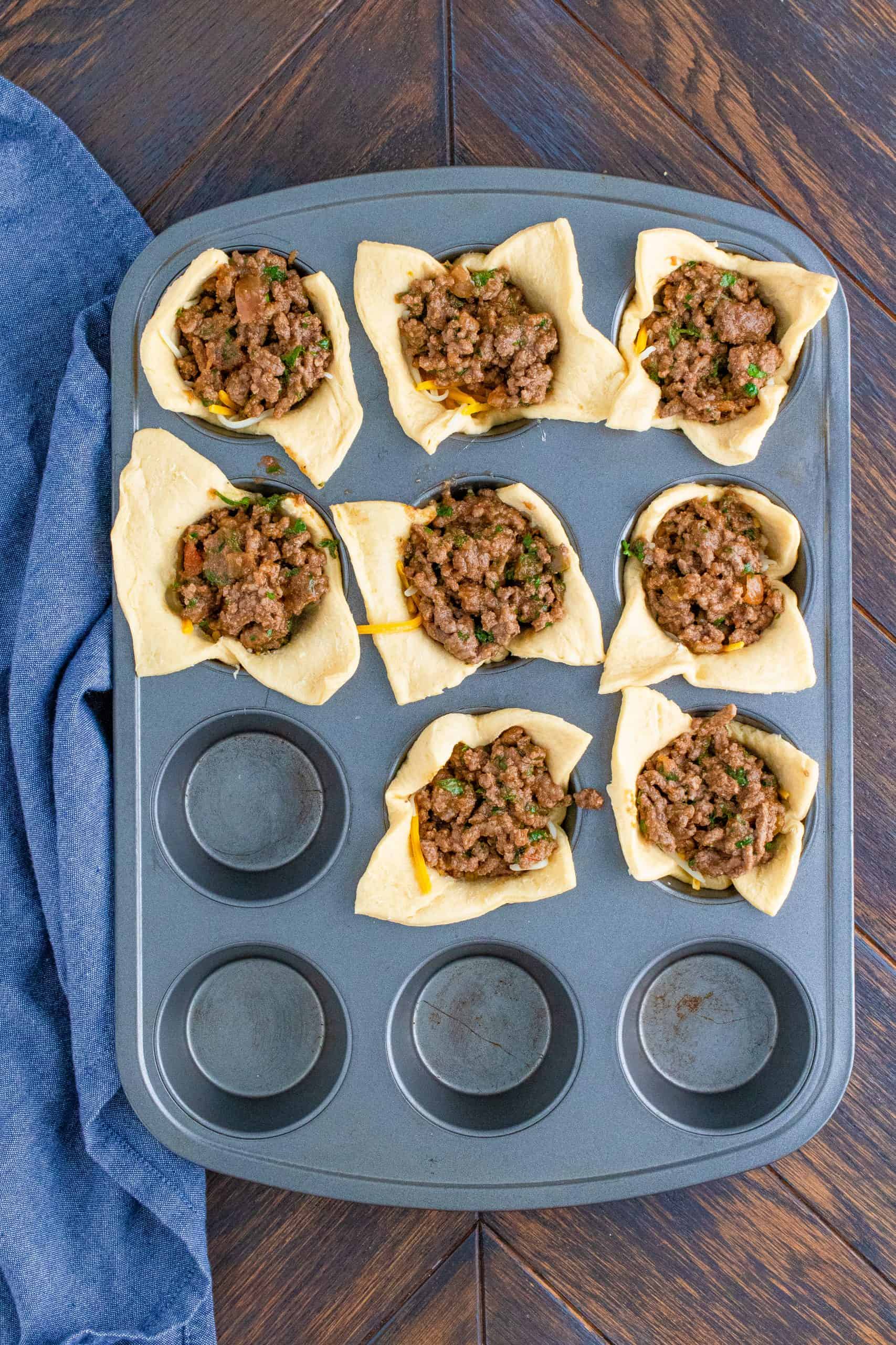 Taco meat added over cheese in muffin tin.