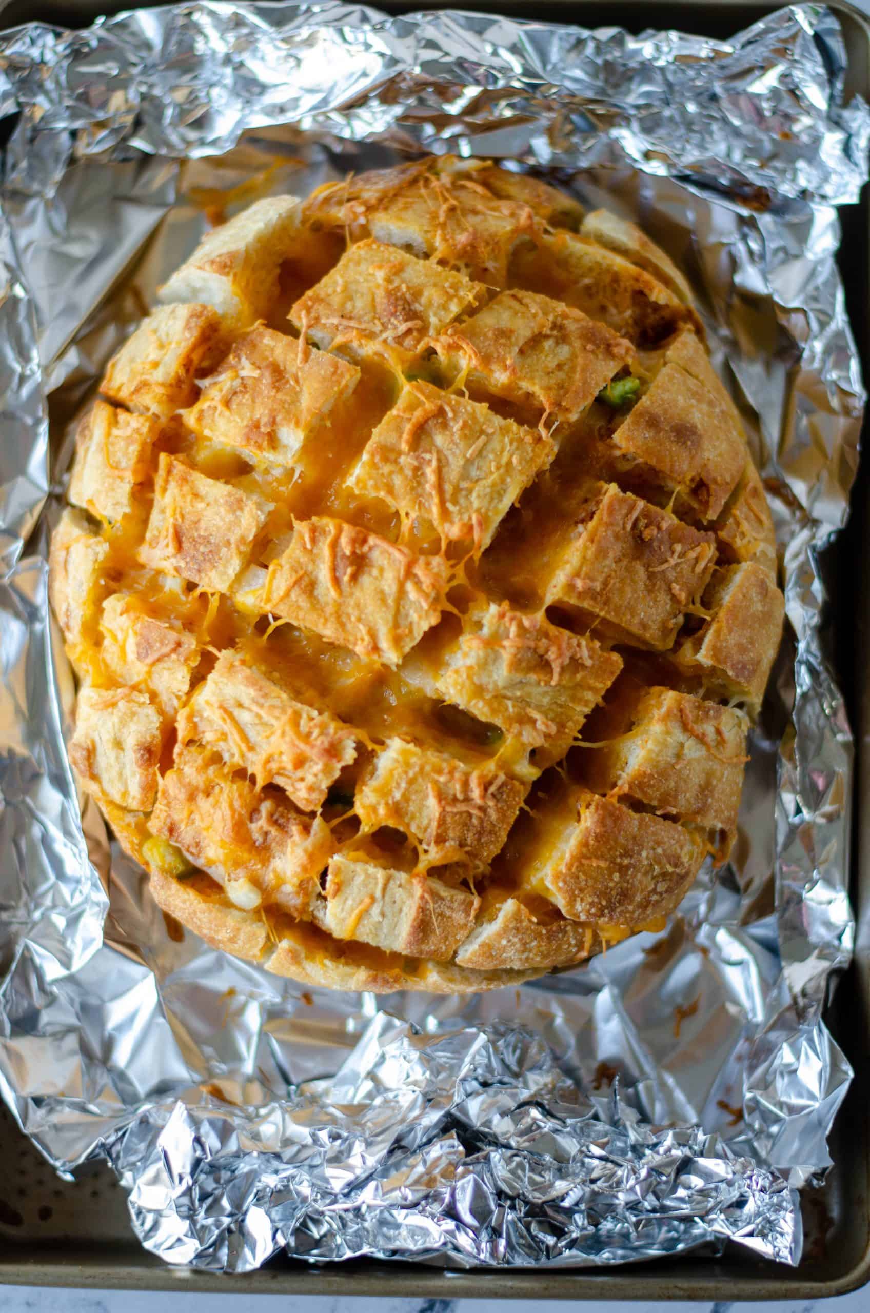 Finished Taco Pull apart bread in foil showing melted cheese in cut portions of loaf.