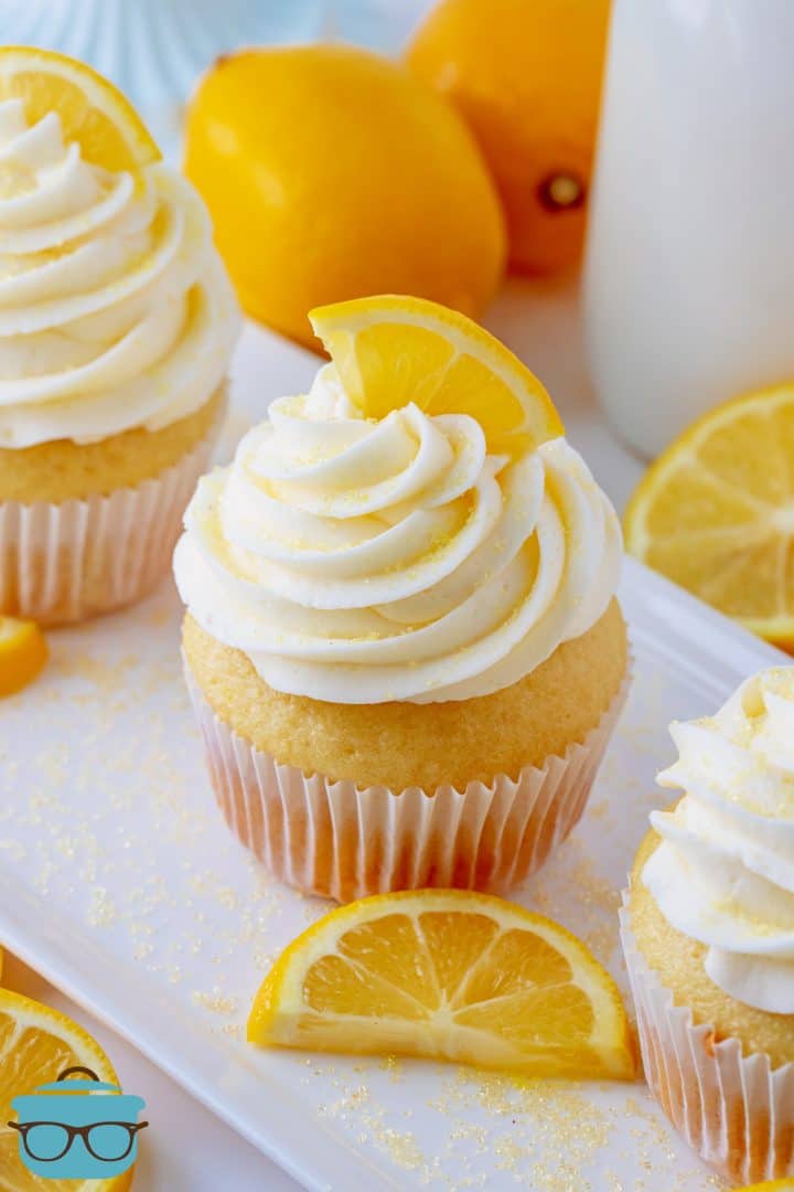 Close up of one Homemade Lemon Cupcake on white patter with lemons in background.