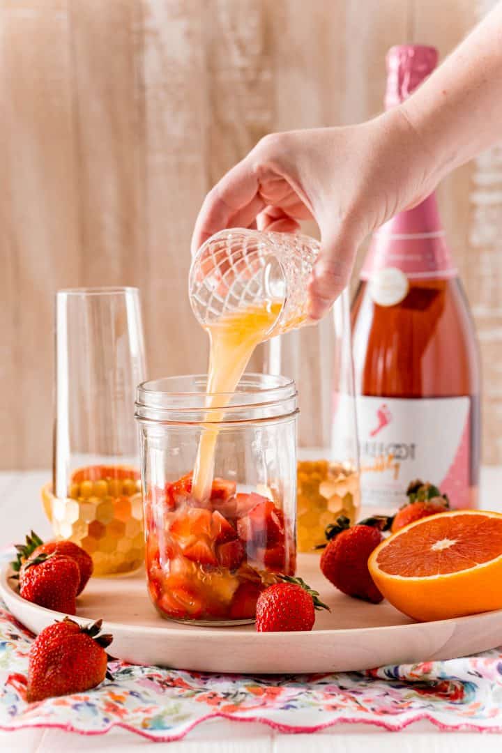 Orange juice being poured into jar with diced strawberries.