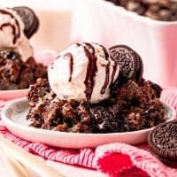 Square image of Oreo Dump Cake on white plate close up with ice cream and chocolate syrup