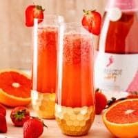 Square image of mimosas with strawberry garnish on glasses