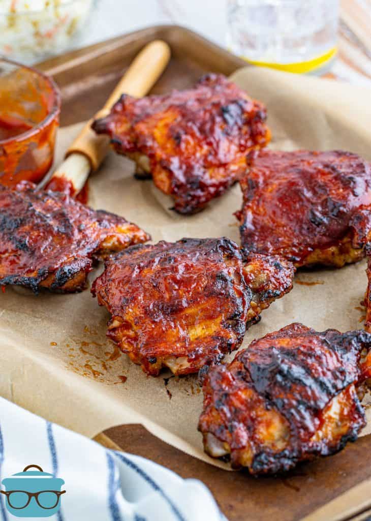 Grilled BBQ Chicken Thighs on parchment lined pan with dabber and bbq sauce